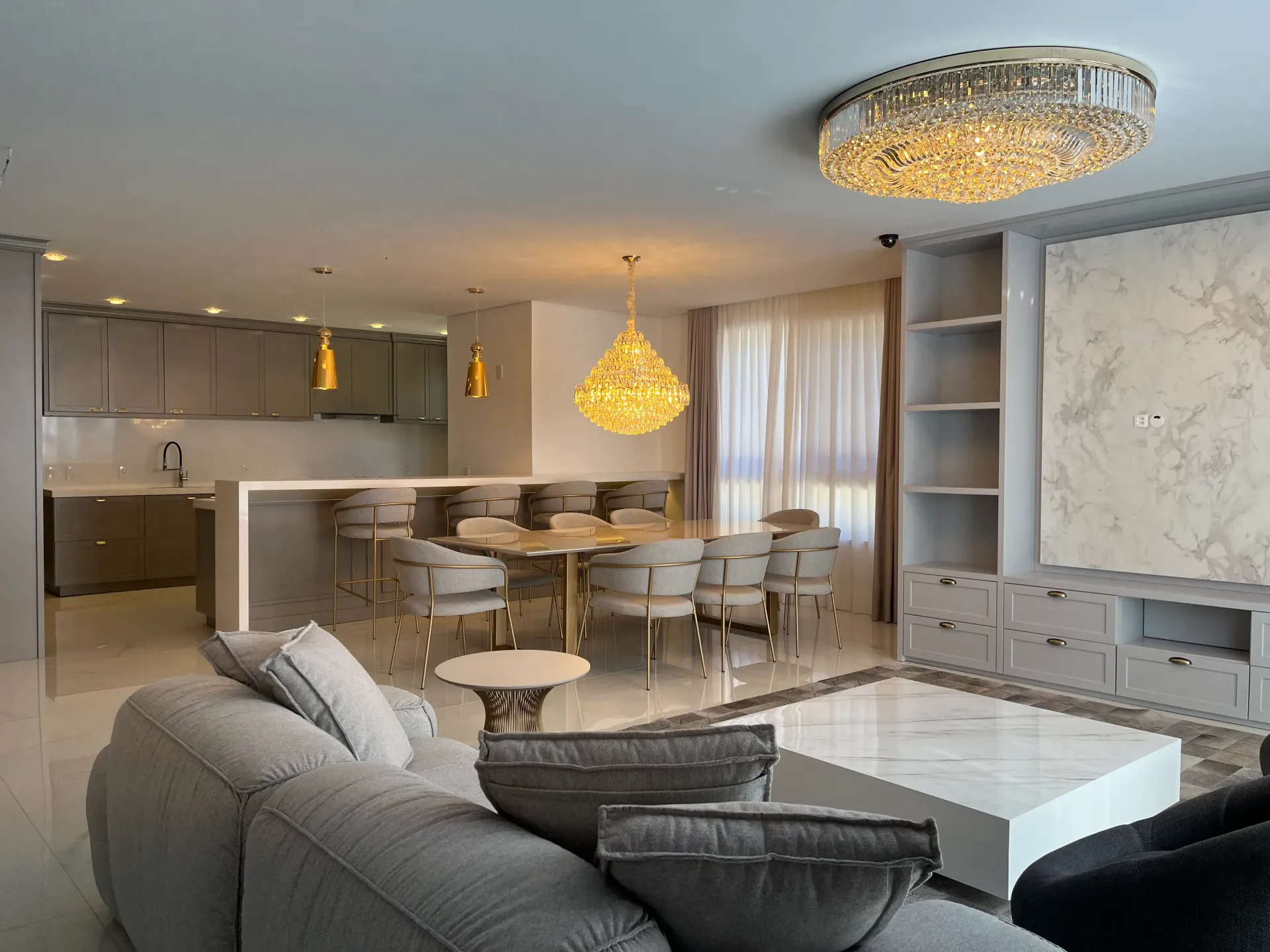 Sala de estar moderna com cozinha integrada, detalhes em mármore e iluminação com lustre.