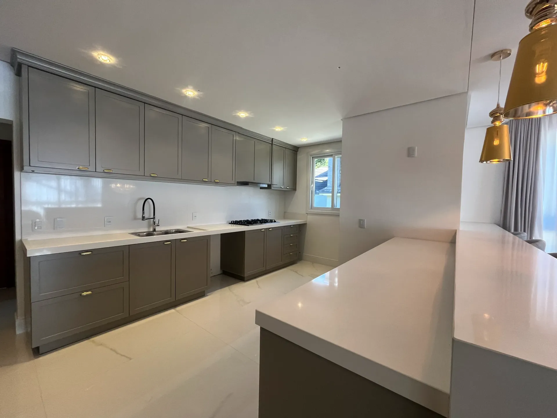 Cozinha moderna com armários cinza, bancadas brancas e balcão com banquetas.