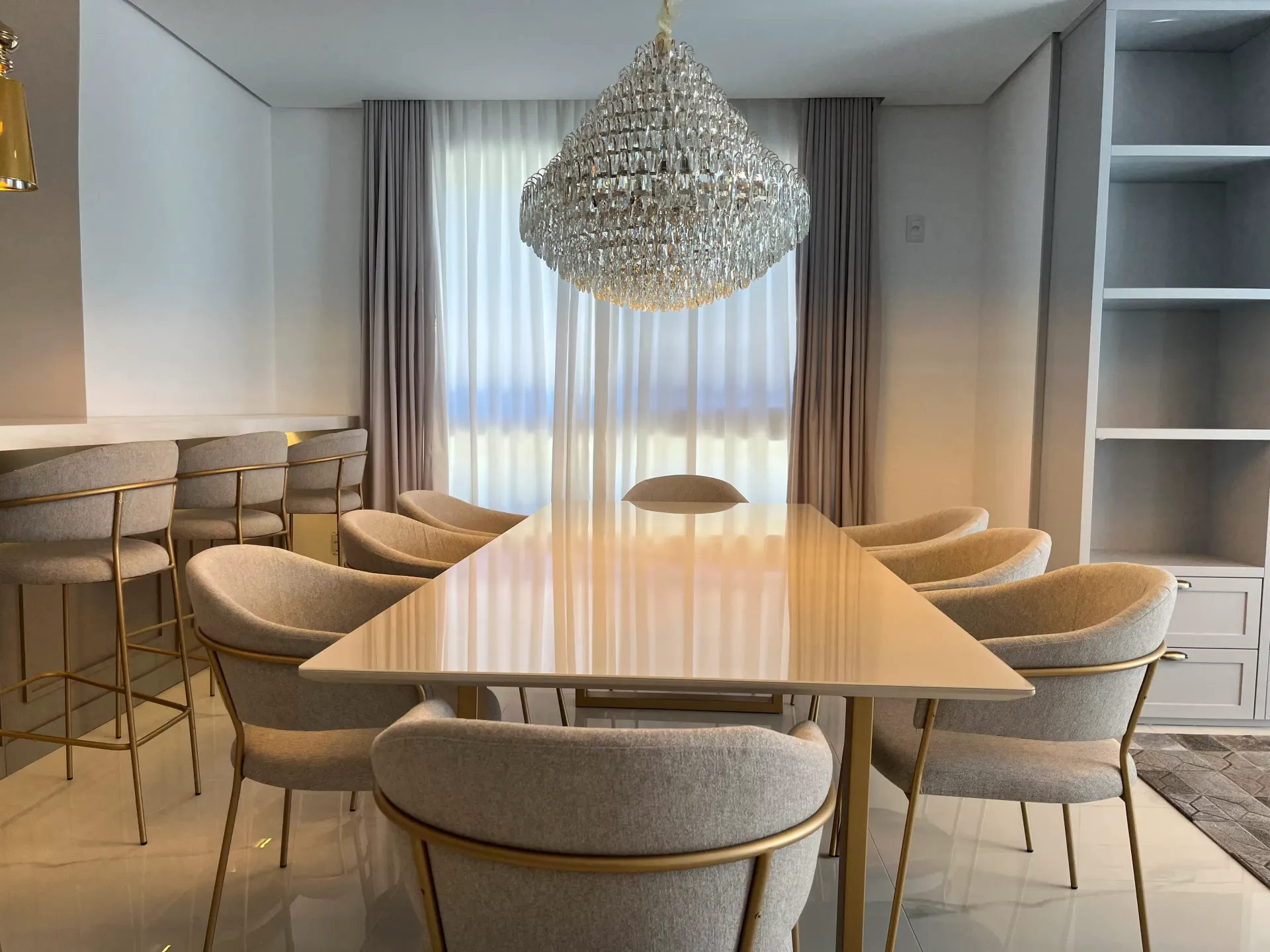 Sala de jantar elegante com lustre, mesa comprida e cadeiras estofadas.