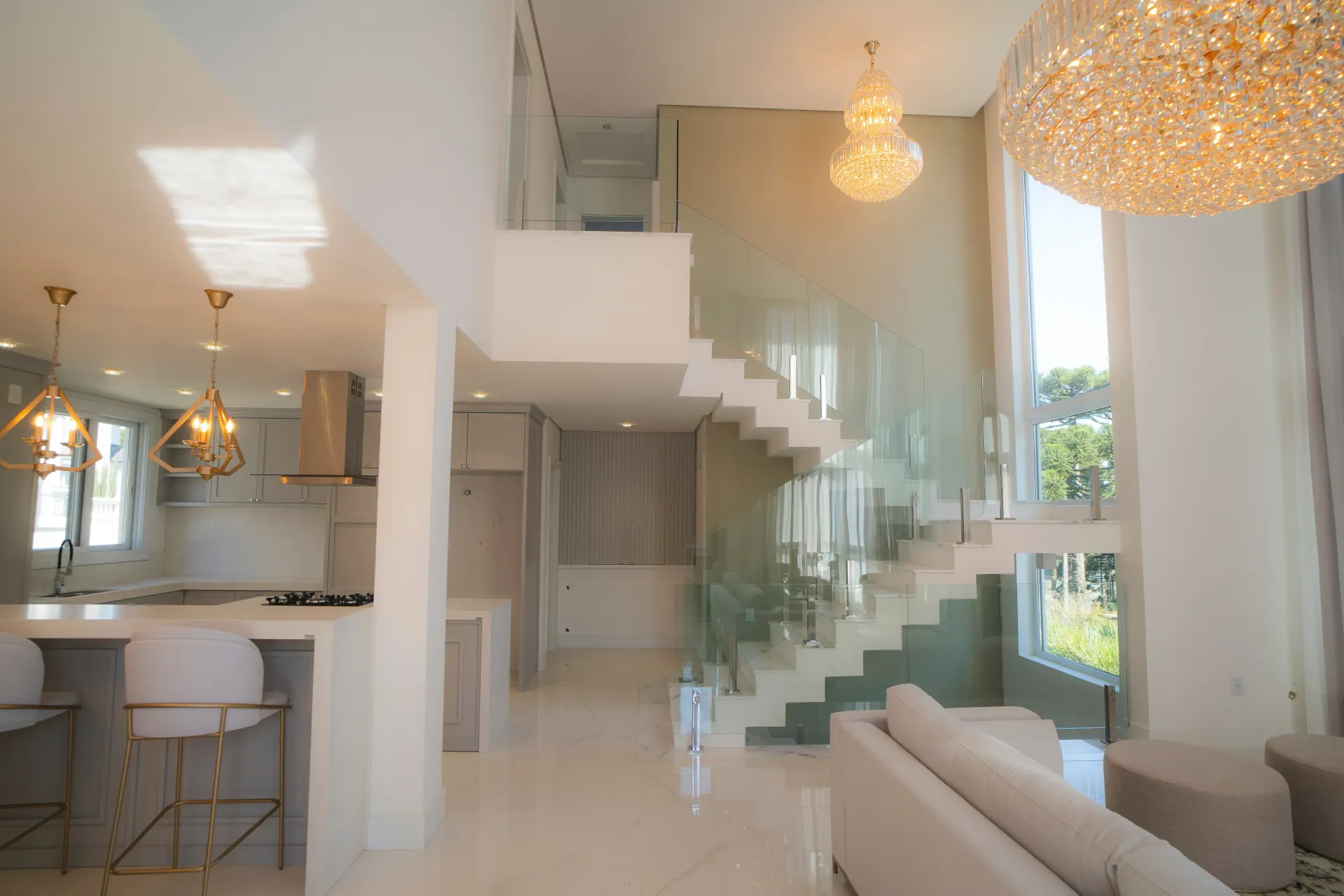 Interior de casa moderna de conceito aberto com escada, cozinha e sala de estar. Espaço amplo e luminoso com lustres.