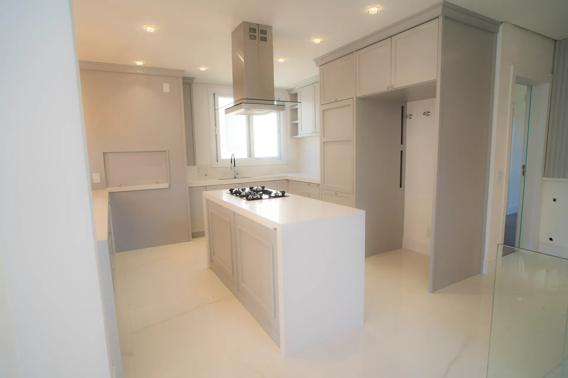 Cozinha moderna branca com ilha e eletrodomésticos embutidos, interior luminoso.