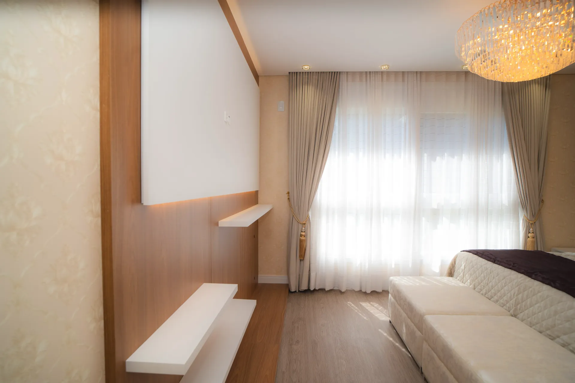 Quarto com painéis de madeira, prateleiras brancas, cortinas transparentes e um lustre decorativo.