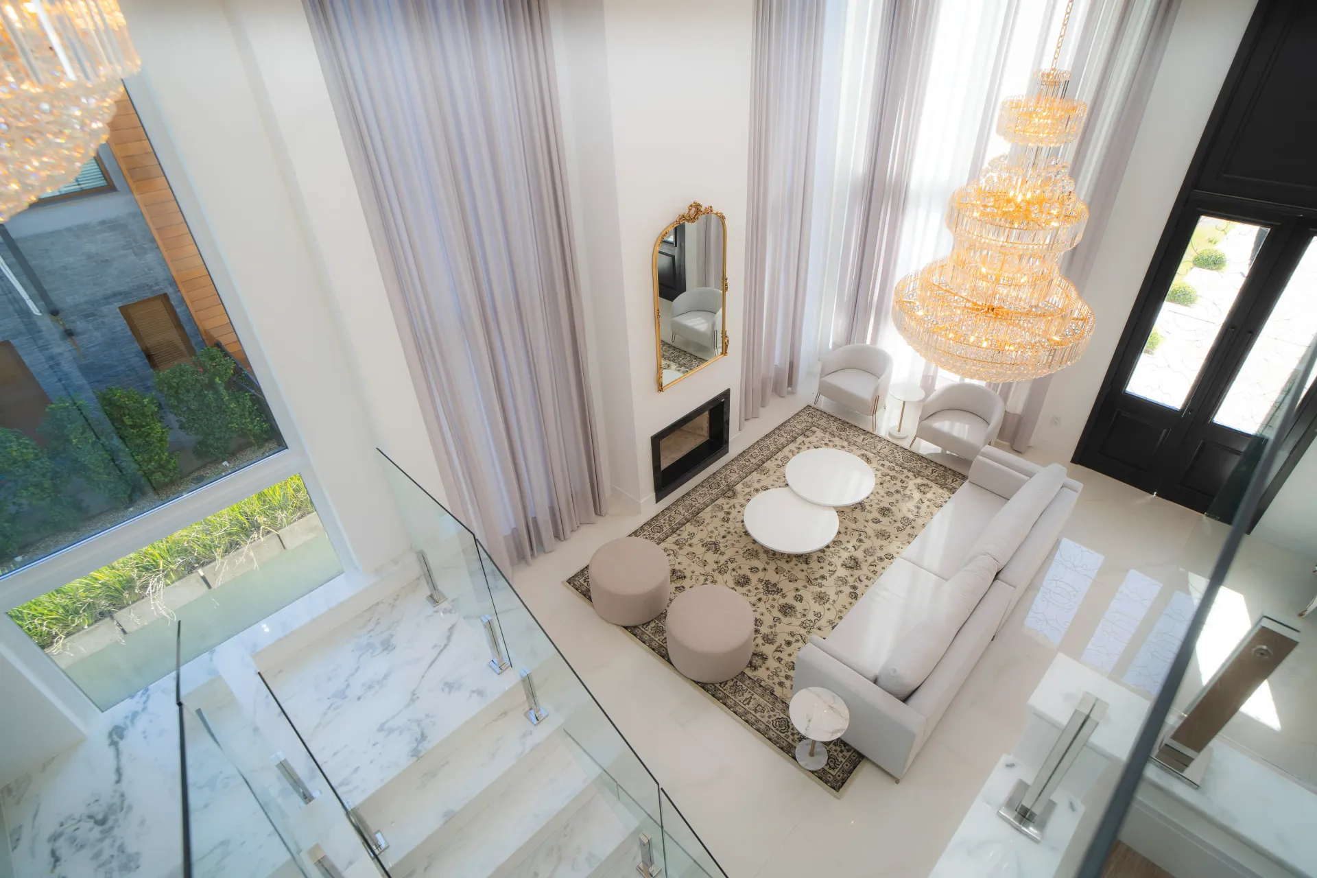 Vista de cima de uma sala de estar moderna com pé-direito alto, lareira e um grande lustre.