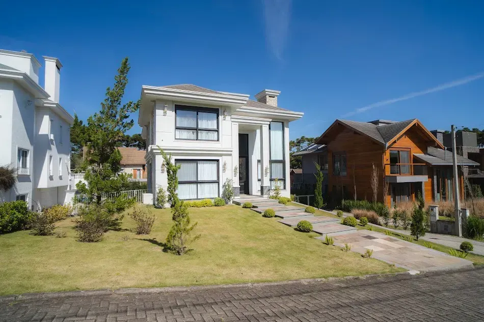 Casa branca de dois andares com caminho de pedra e gramado em um dia ensolarado.