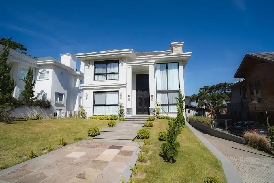 Casa branca de dois andares com caminho de pedra e gramado em um dia ensolarado.