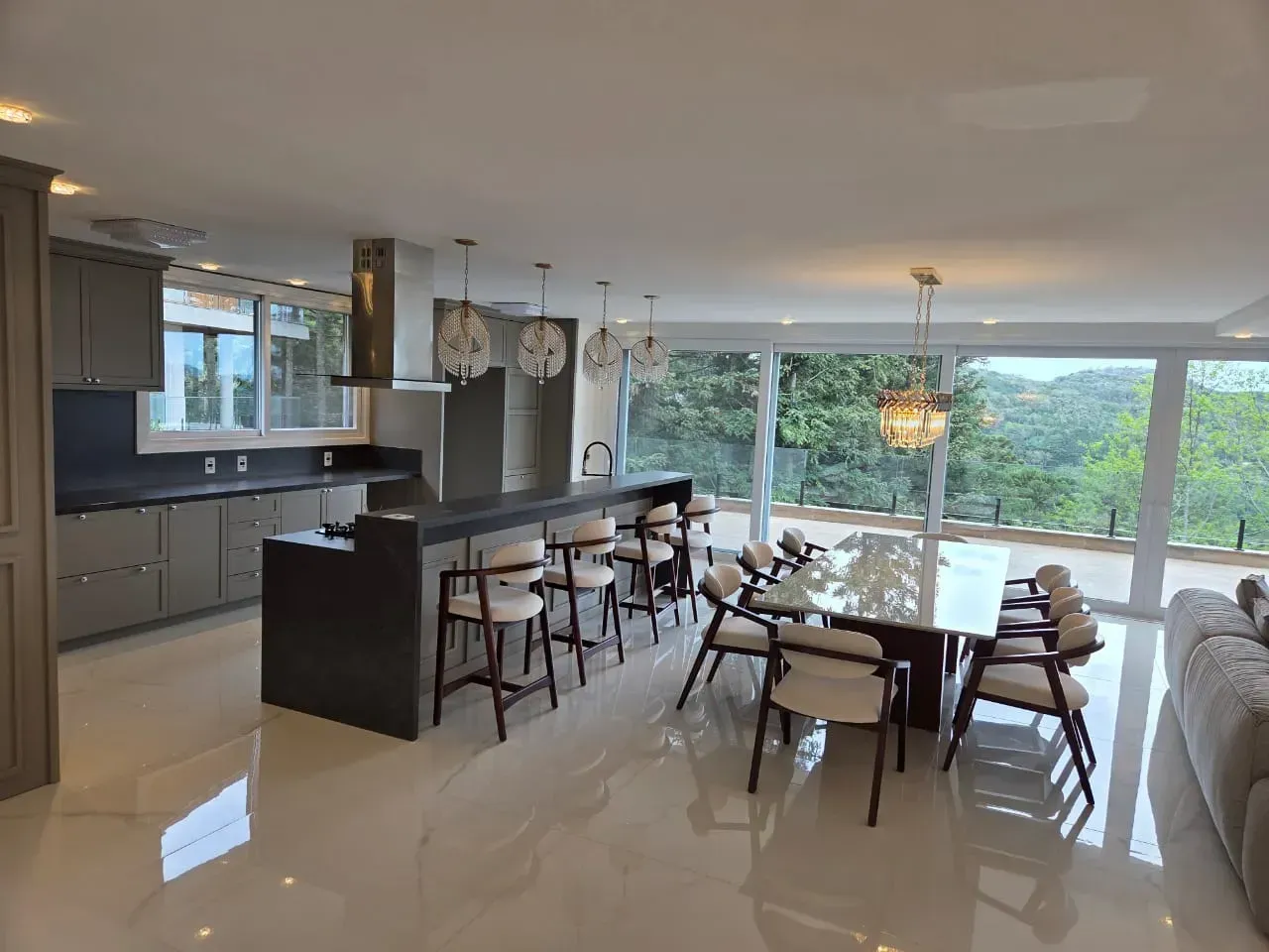 Cozinha moderna com ilha, banquetas, área para refeições e grandes janelas com vista para as árvores.