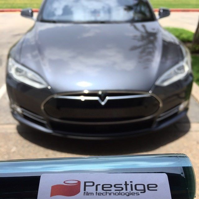 A grey Tesla Model S with tinted windows, parked outdoors with Prestige film roll in foreground.