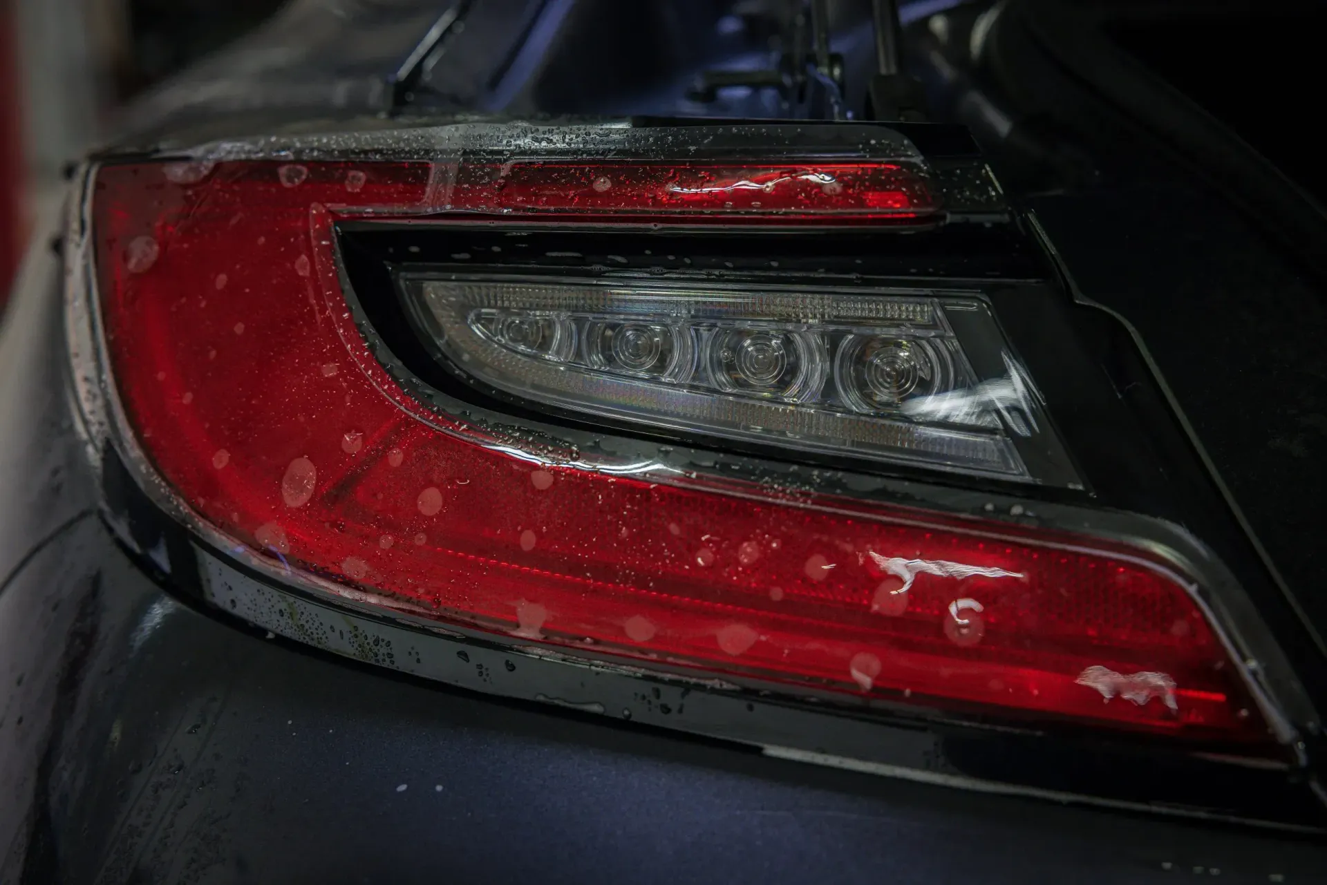 Close-up of a dark blue car's taillight with condensation. The light is red and white, with a sleek, modern design.