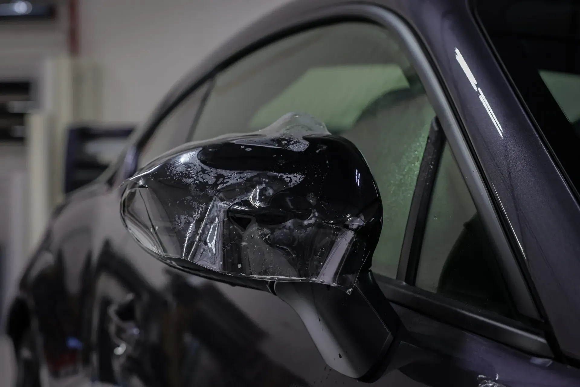 Black car side mirror with protective film being applied.