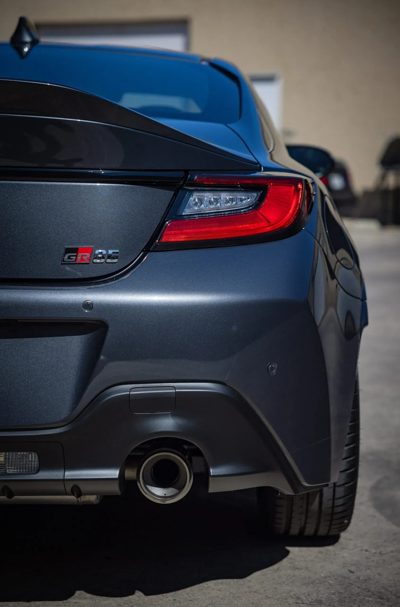 Rear view of a gray Toyota GR86 sports car with a red taillight and exhaust pipe.