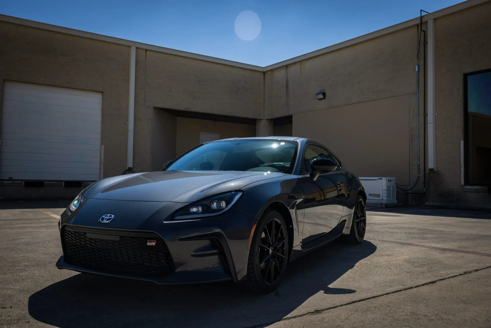 Dark gray sports car parked in front of a beige building on a sunny day.