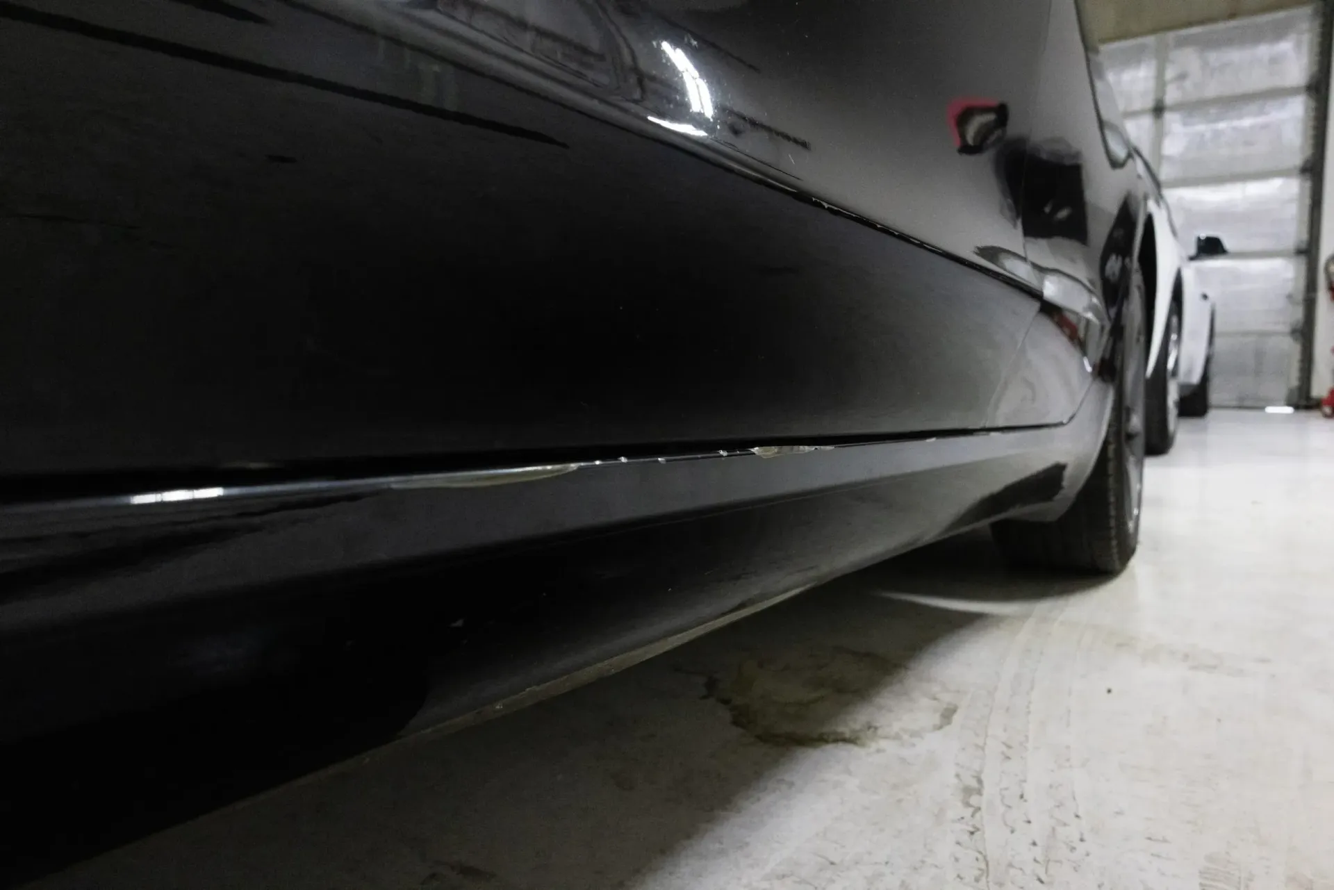 Black car's lower side panel with scratched paint in a well-lit garage.