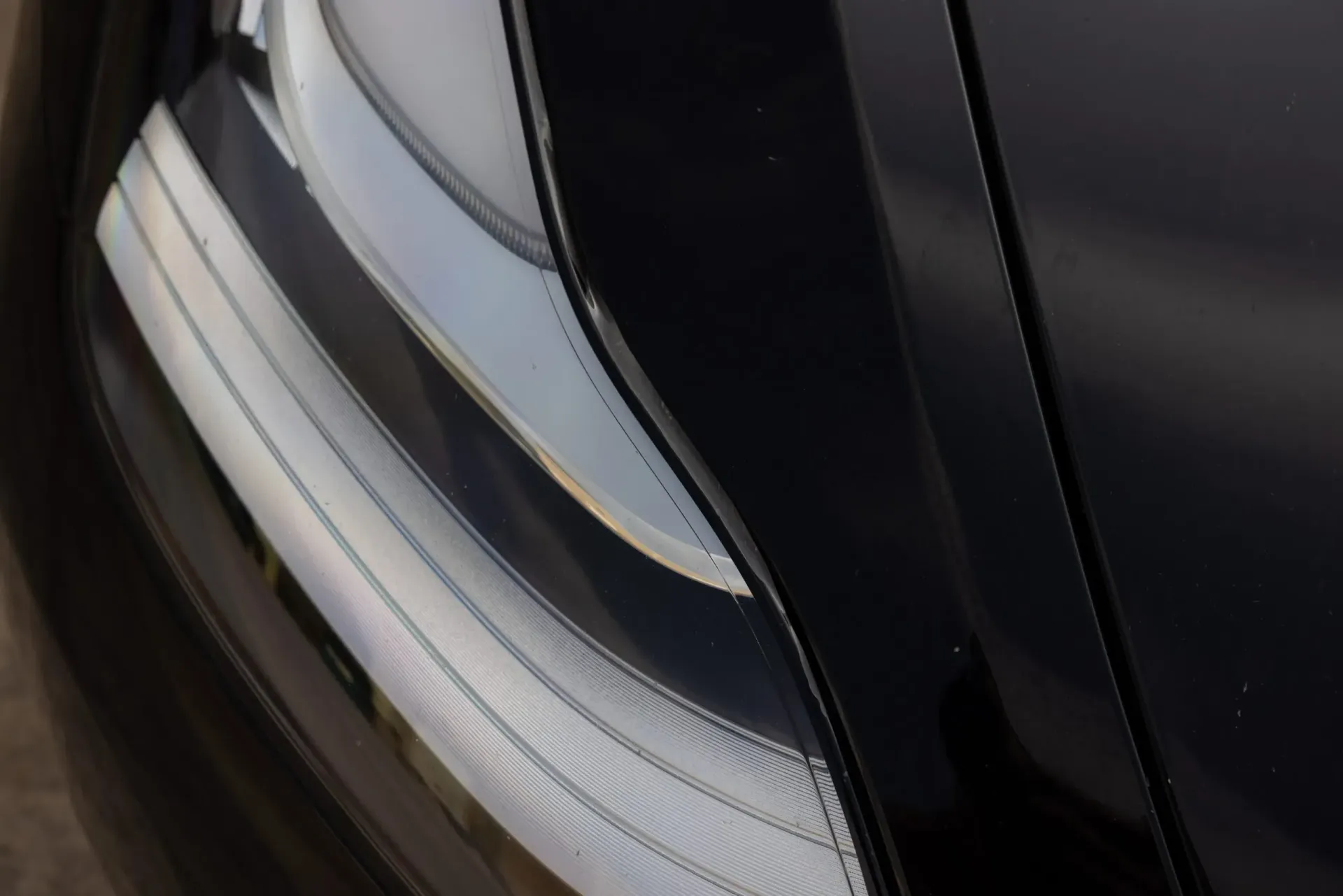 Black car headlight with a sleek, modern design, angled against a glossy black surface.