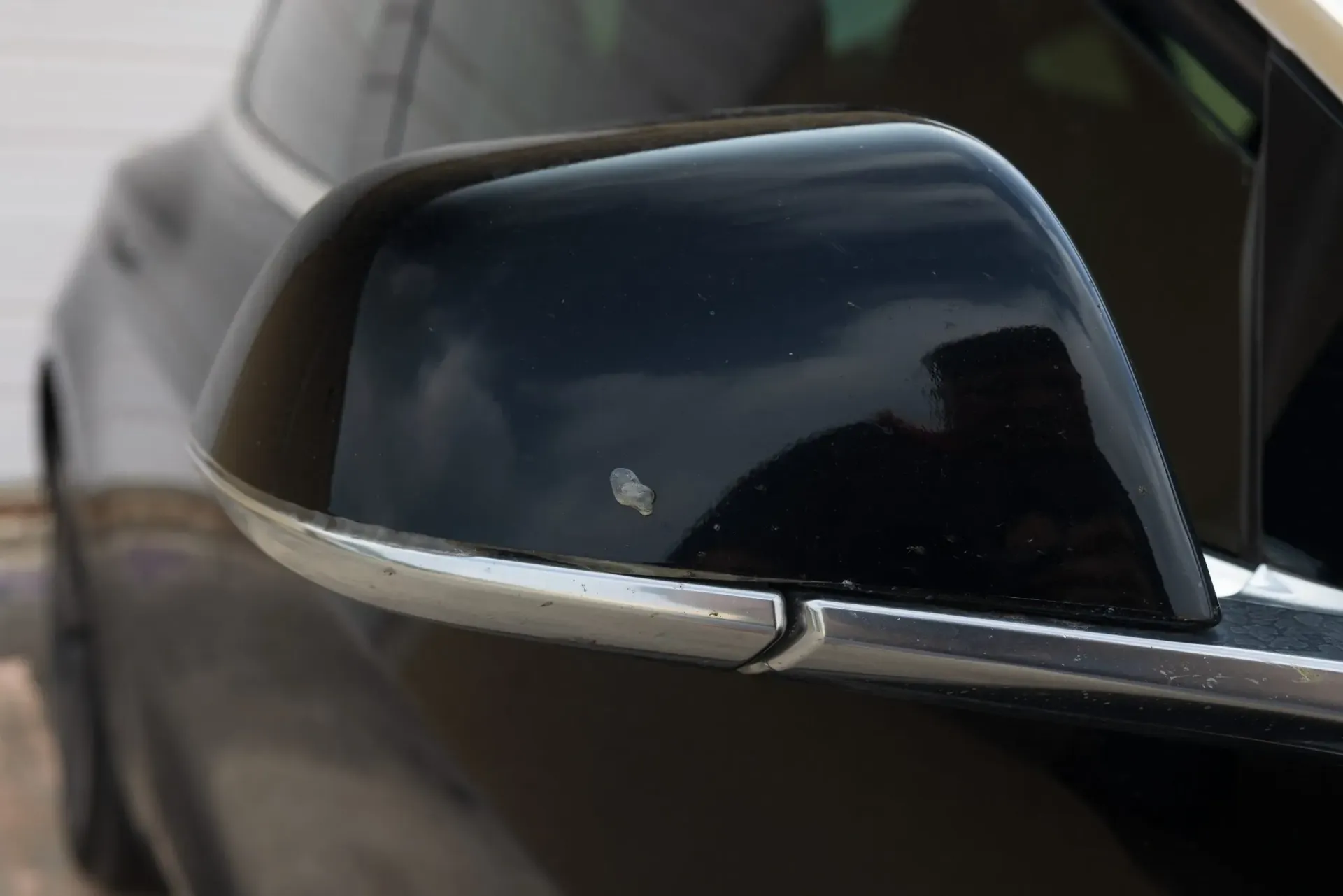 Black car side mirror with a small paint chip, in an outdoor setting.