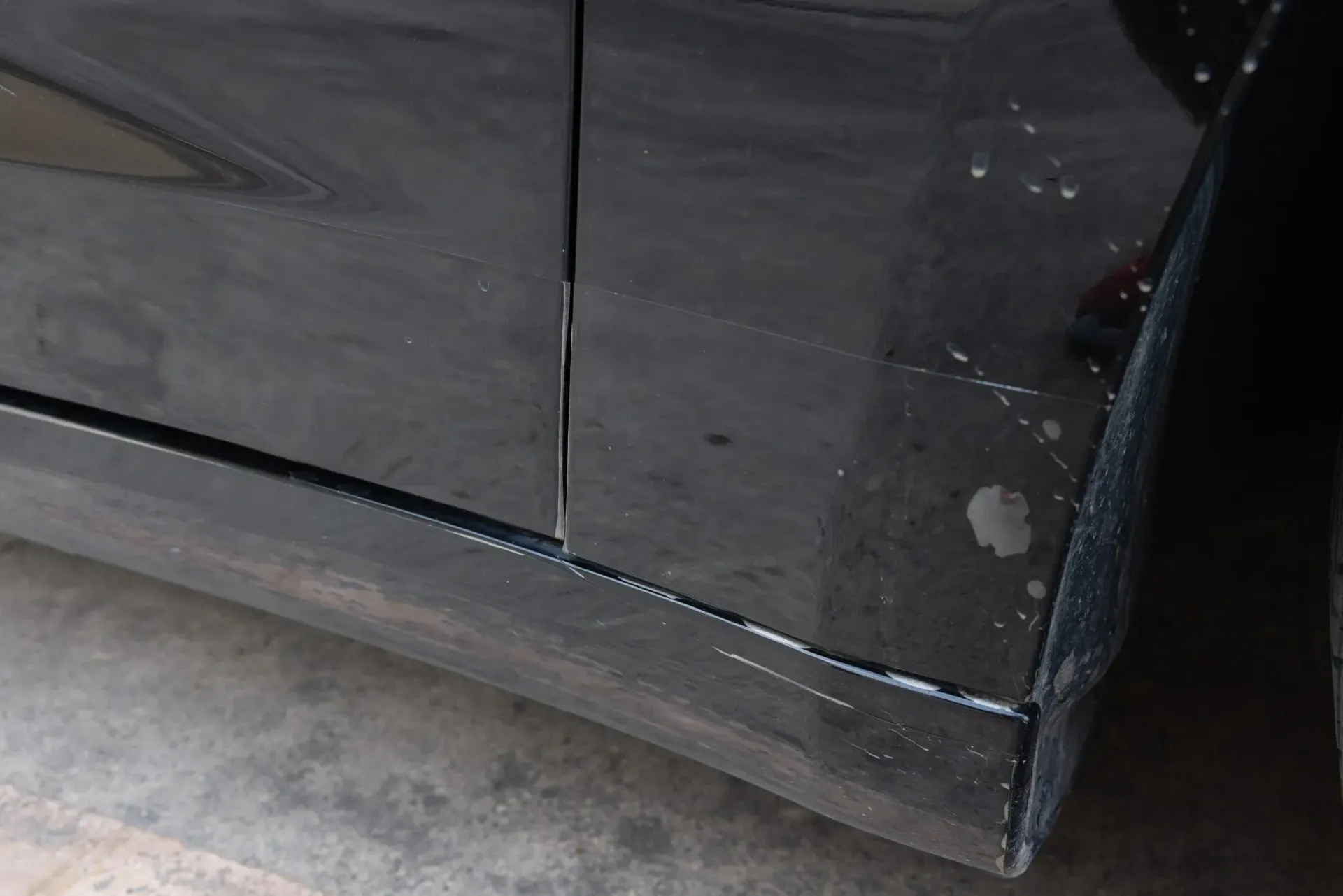 Close-up of a black car door. The door has visible scratches and what appears to be paint residue along the bottom edge.