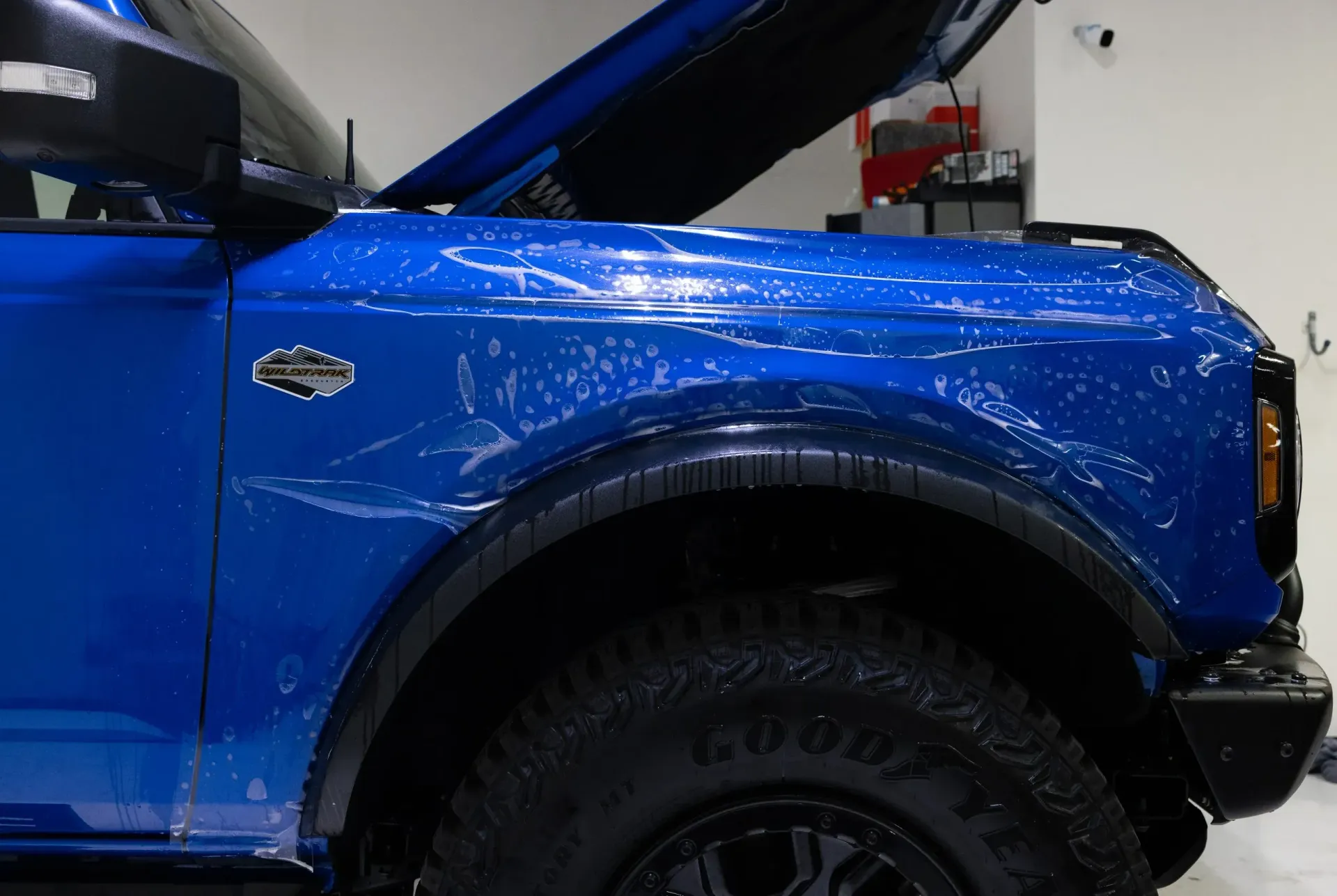 Blue Ford Bronco, hood open, covered in protective film, in a shop.