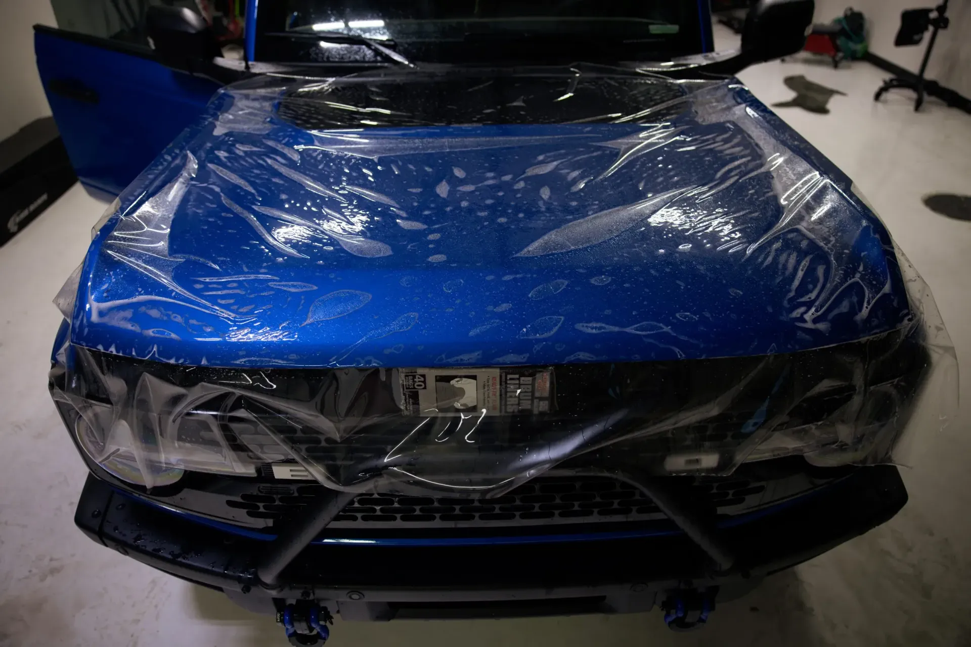 Blue car with clear protective film on the hood, indoors.