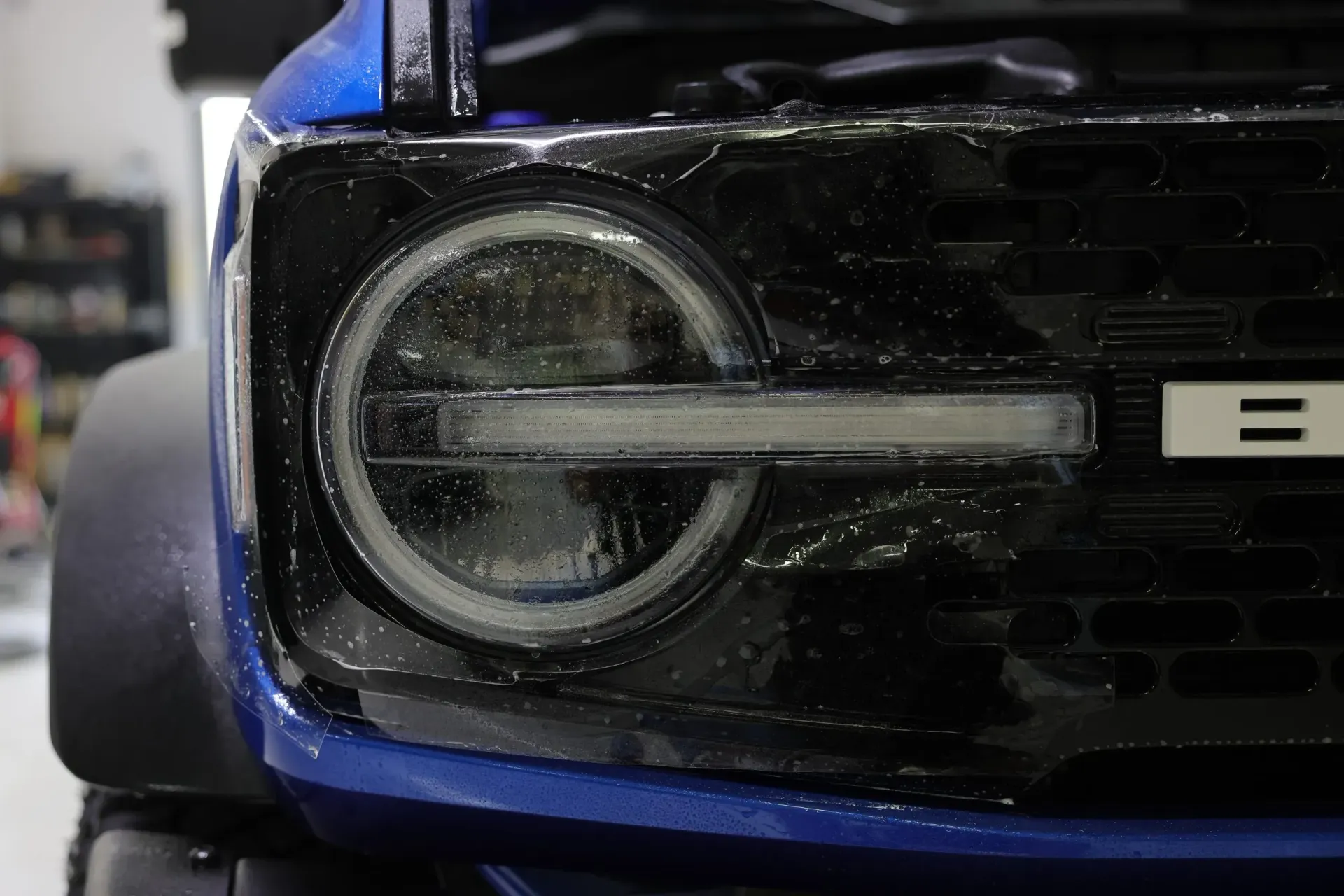 Close-up of a blue Ford Bronco headlight with a white halo light.
