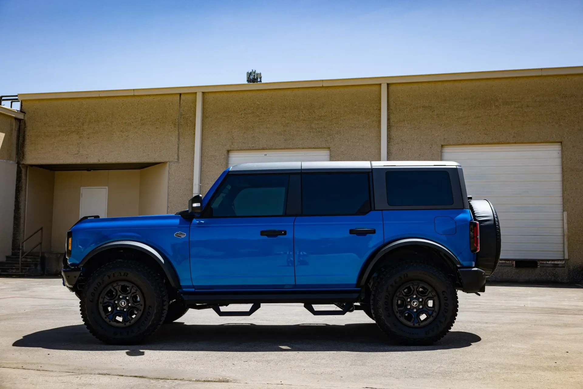 Blue Ford Bronco parked next to a tan building with black tires.