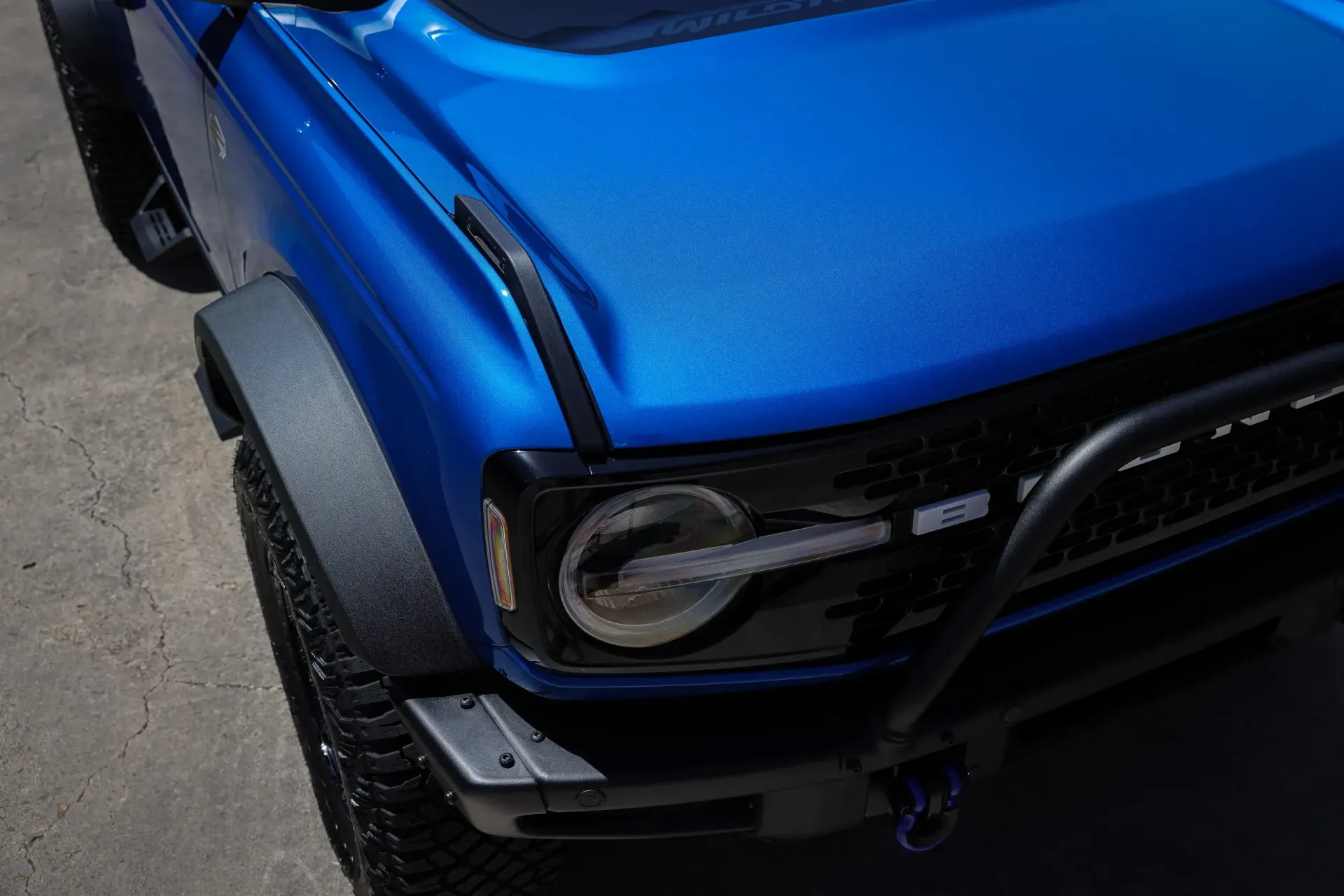 Blue Ford Bronco front end, black accents, textured fender and hood, outdoor.