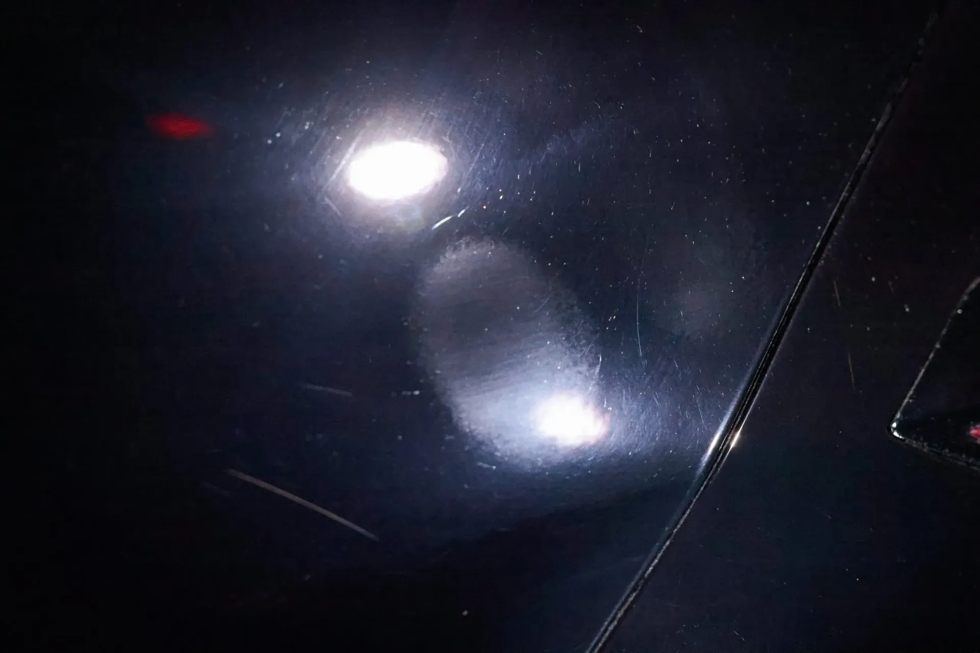 Black surface reflecting bright light, with lighter patches and possible imperfections.