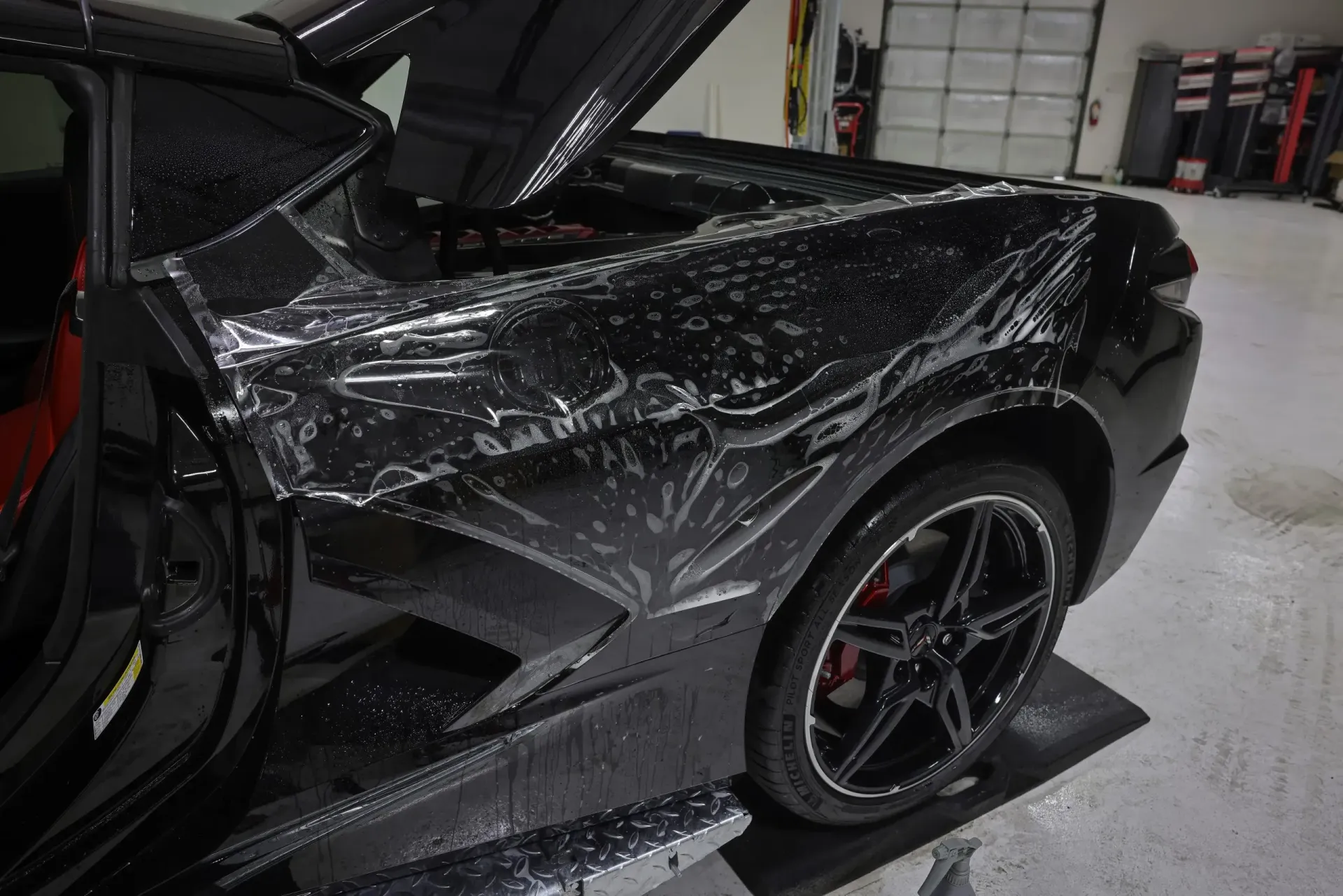 Black sports car with protective film applied, in a garage.