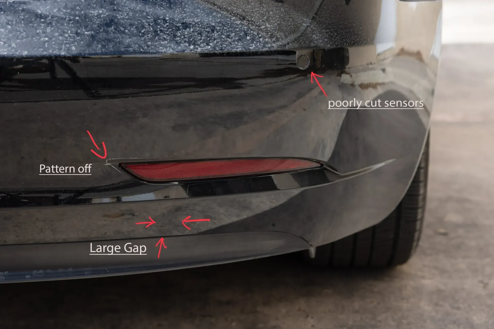 Black car bumper with red reflector, panel gaps, and parking sensor.