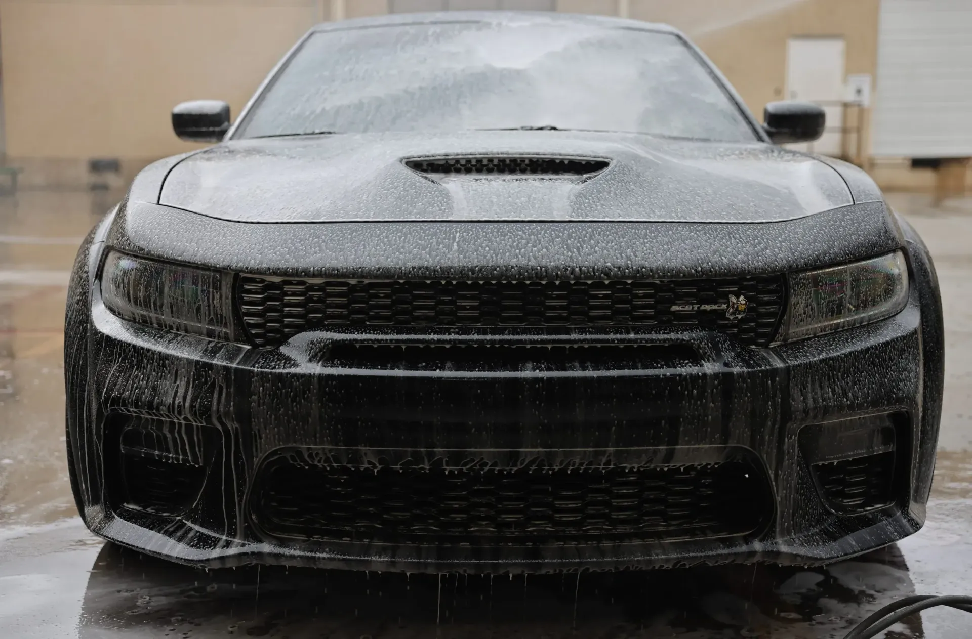 Black Dodge Charger covered in soapy foam, being washed outdoors.