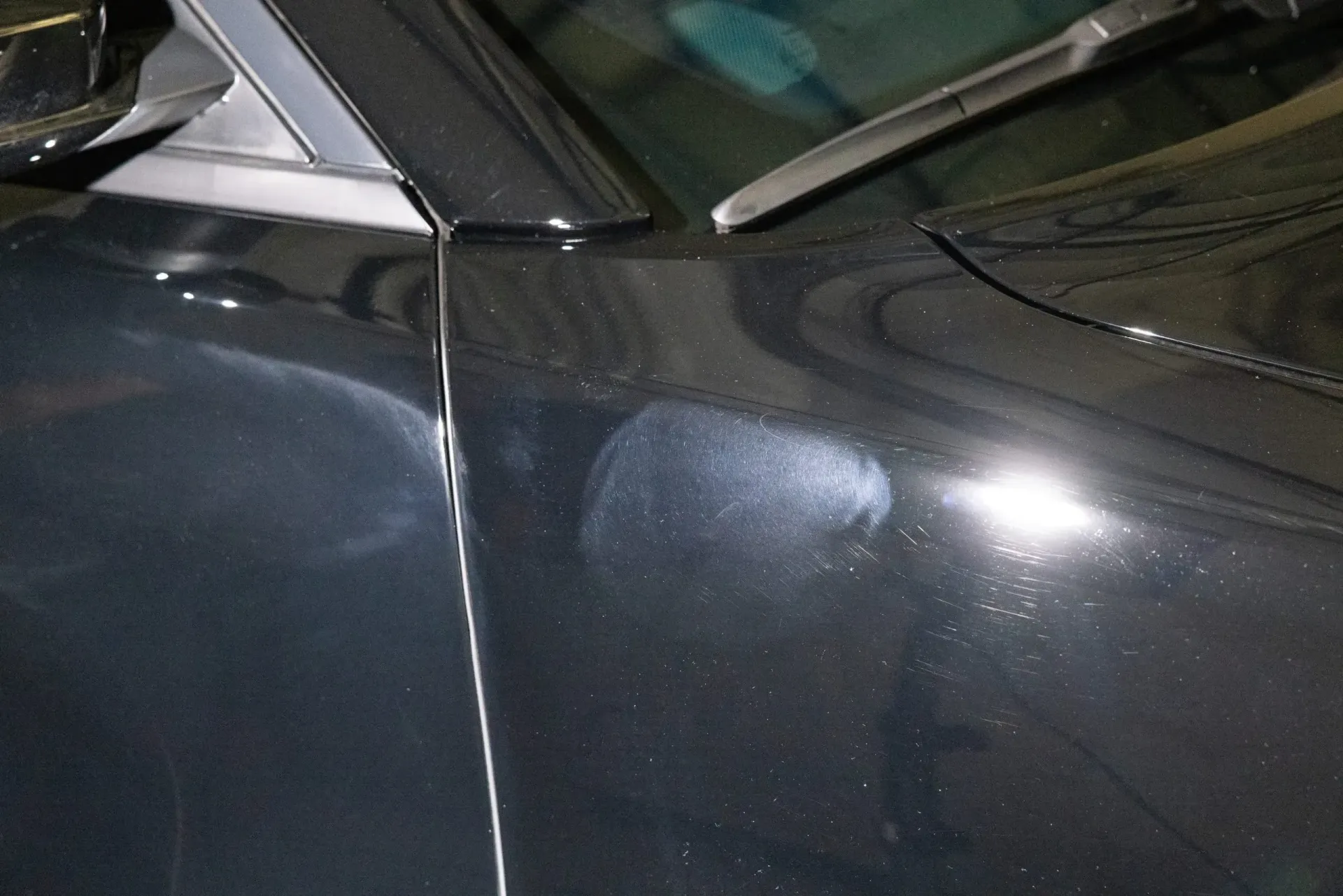 Dark car's front fender with water spots; windshield wiper and part of window visible.