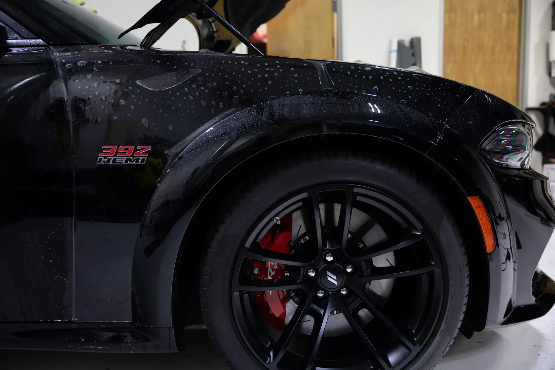 Black Dodge Charger's wet front end, red brake calipers, black wheels, and
