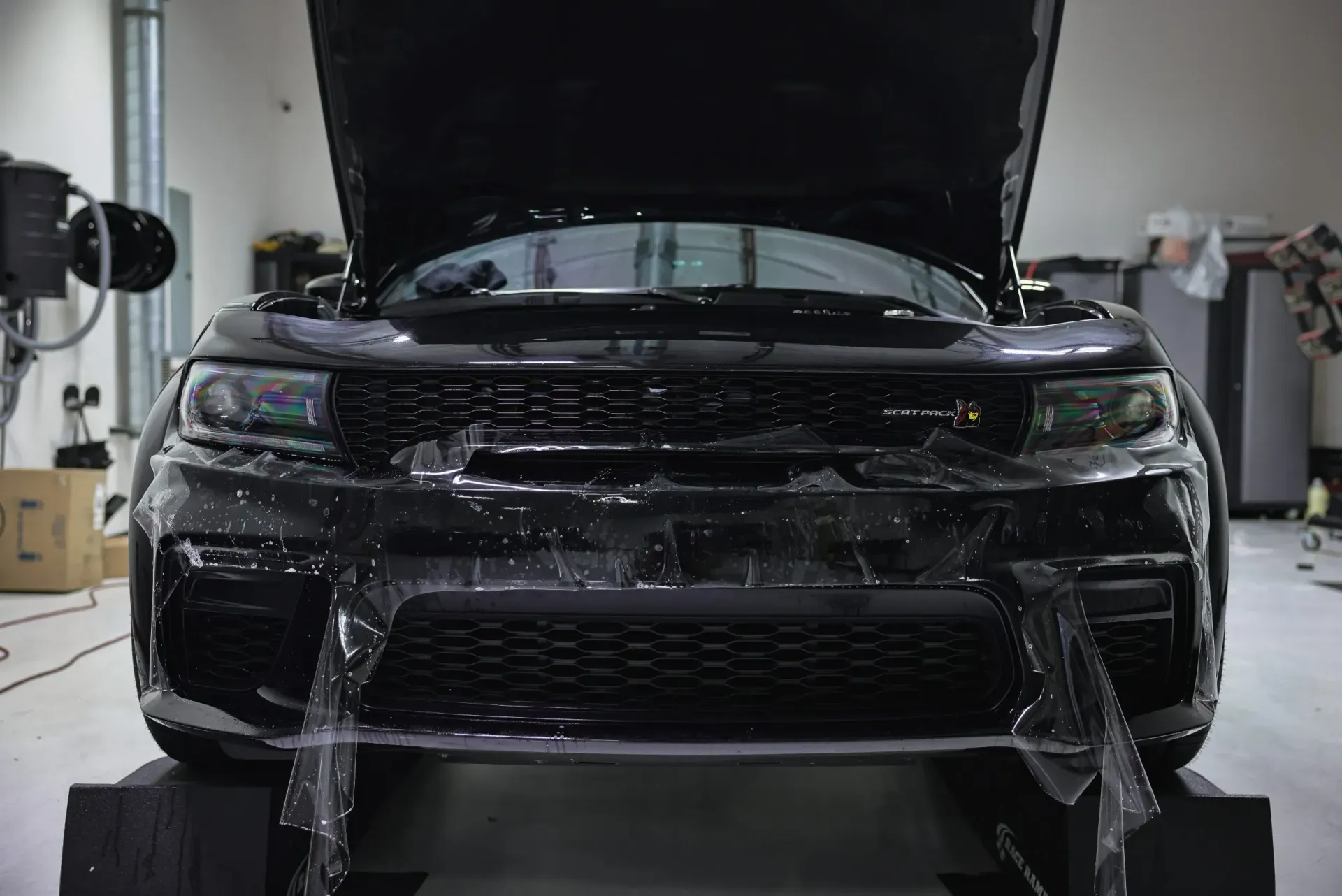 Black SUV with open hood covered in protective film in a garage.