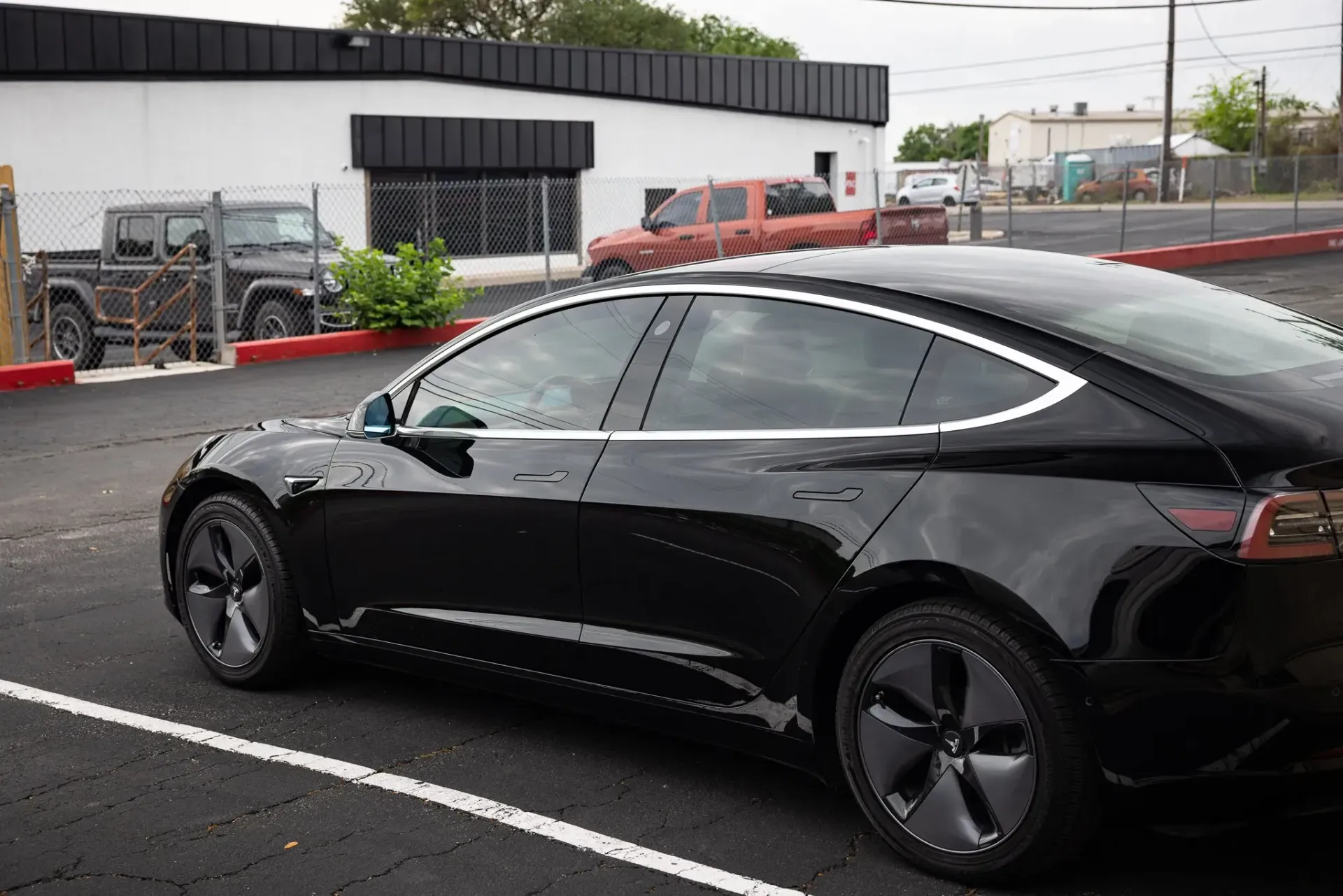 Black Tesla sedan parked in a lot, next to a building.