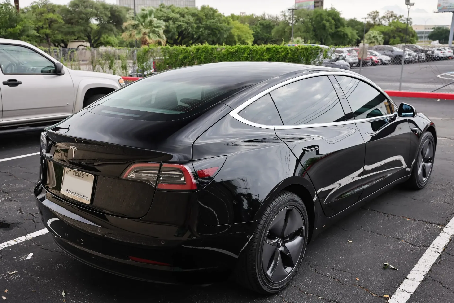 Black Tesla Model 3 parked in a parking lot. The car has tinted windows and black wheels.