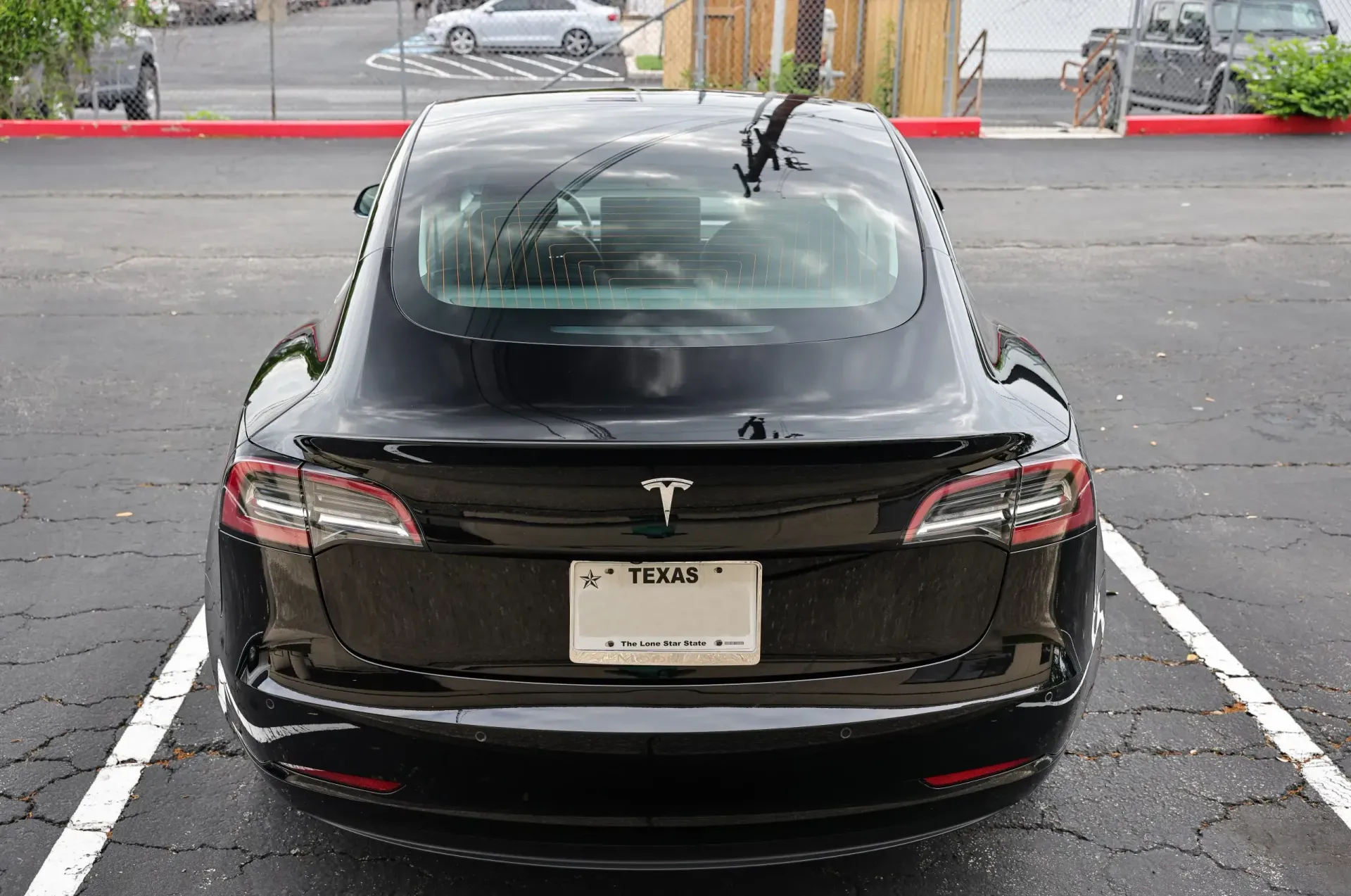 Black Tesla Model 3 parked in a parking spot, viewed from the rear. Texas license plate.