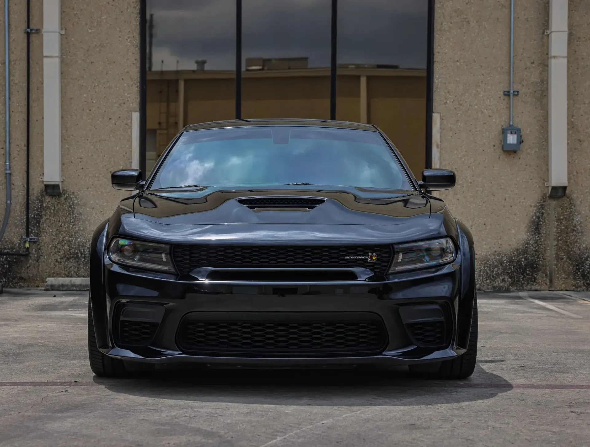 Black Dodge Charger parked in front of a building with glass windows.