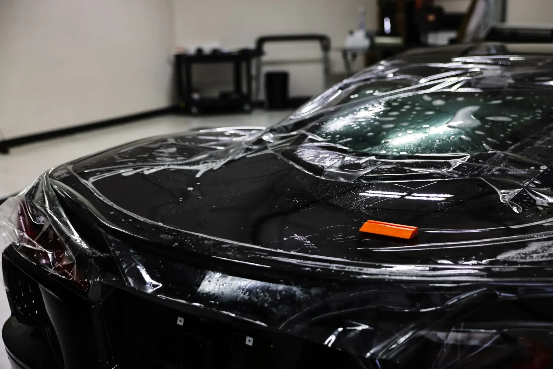 Black car with protective film applied in a garage.