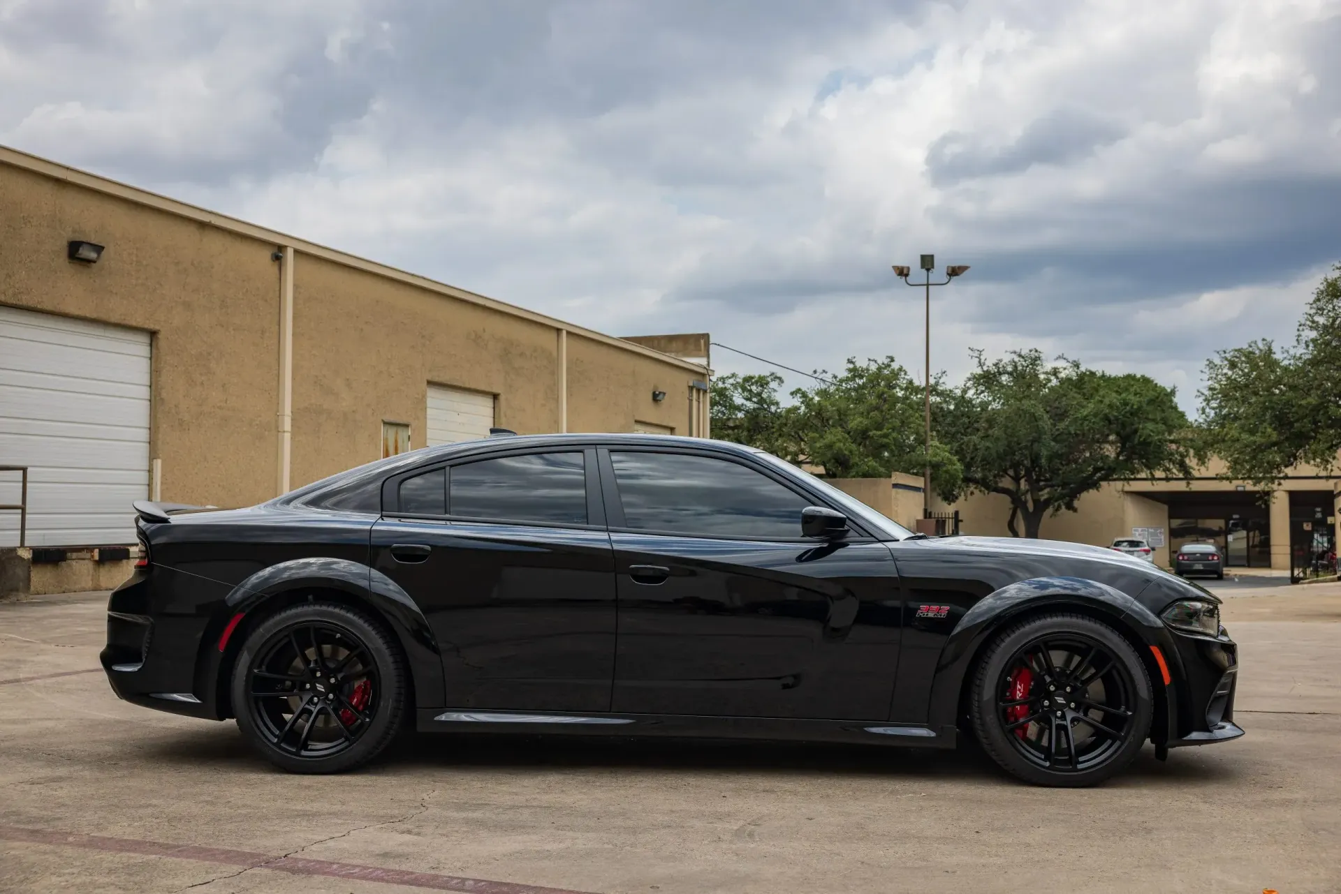 Black Dodge Charger on a street with a tan building and cloudy sky in the background.