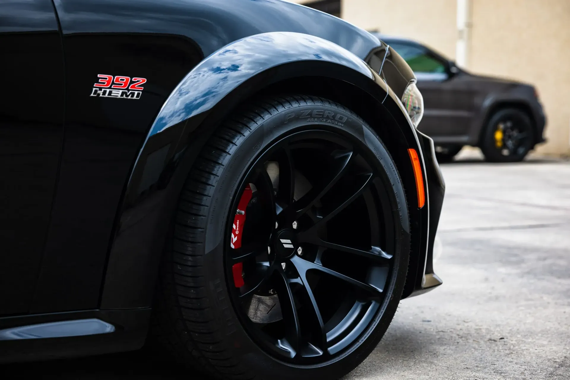 Black car with black rims and red brake calipers; a dark SUV is in the background.