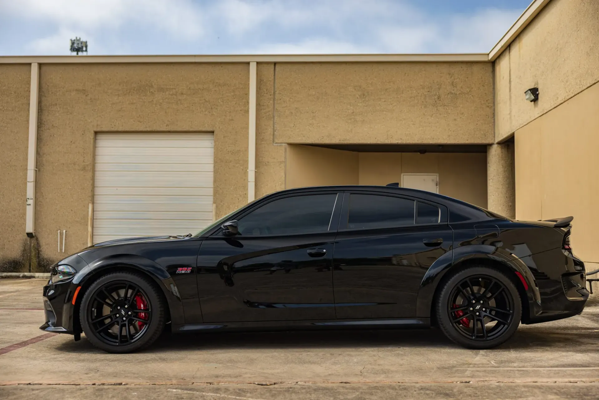 Black Dodge Charger parked outside a tan building, with tinted windows and red brake calipers.