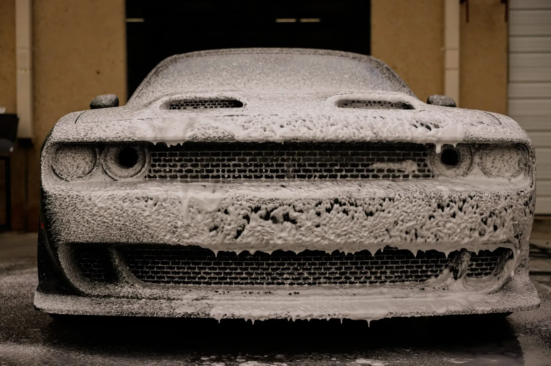 Dodge Challenger covered in thick white foam, in front of a garage.