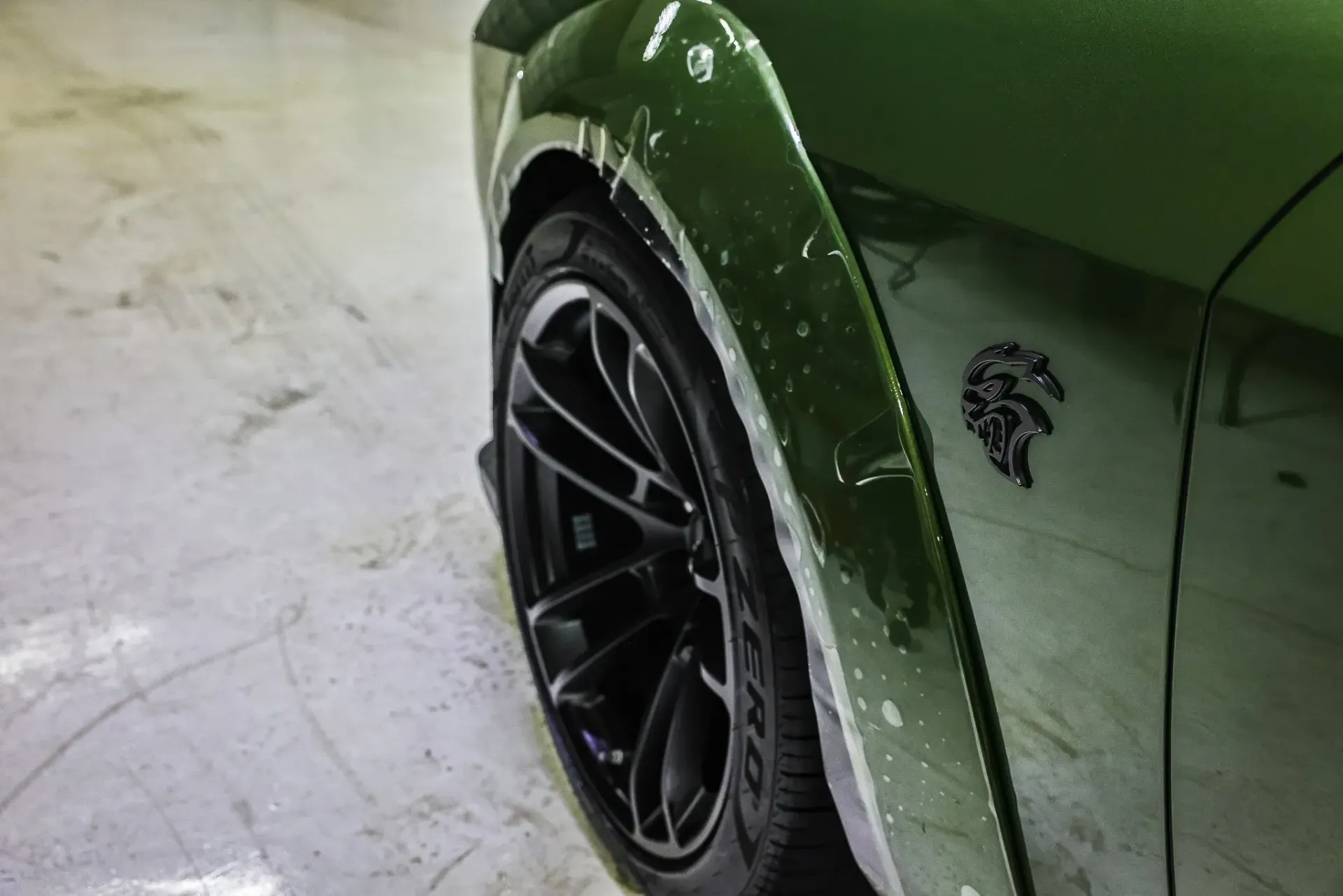 Green Dodge Challenger wheel well, black tire, Demon emblem.
