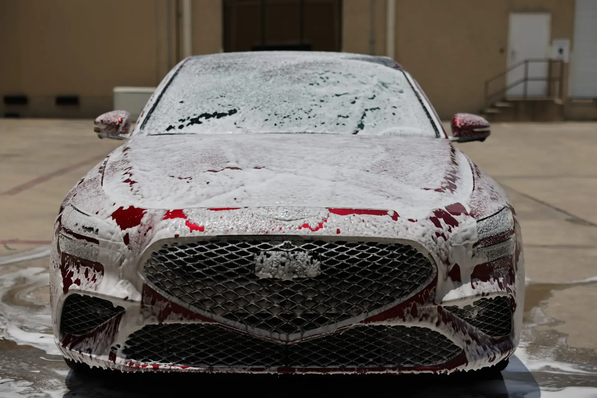 Red car covered in white foam, front view, outdoors.