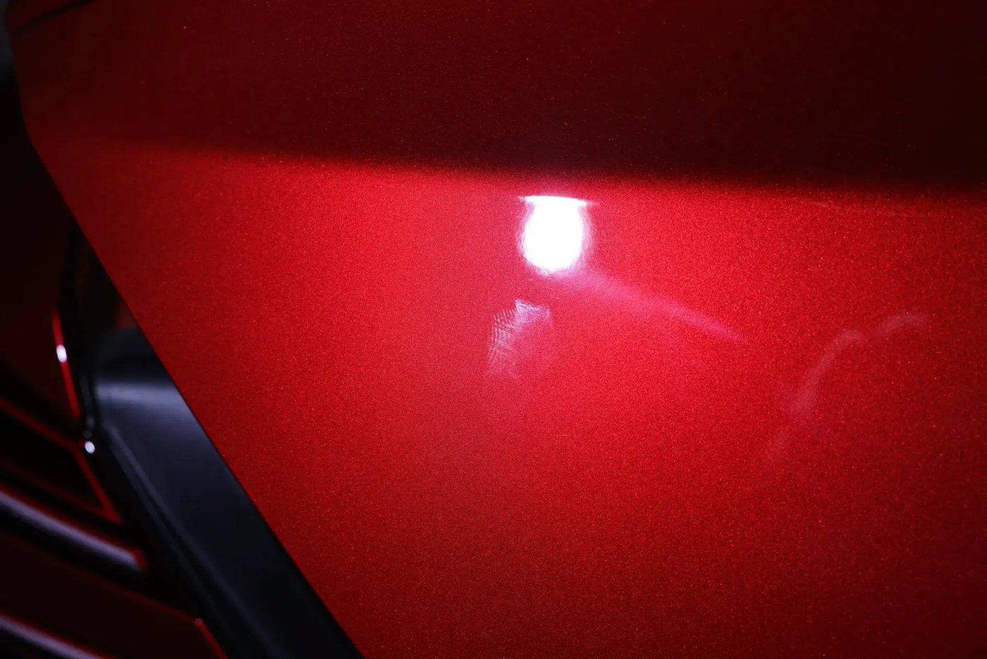 Close-up of a red car door with a shiny, bright spot, possibly indicating a scratch or damage.