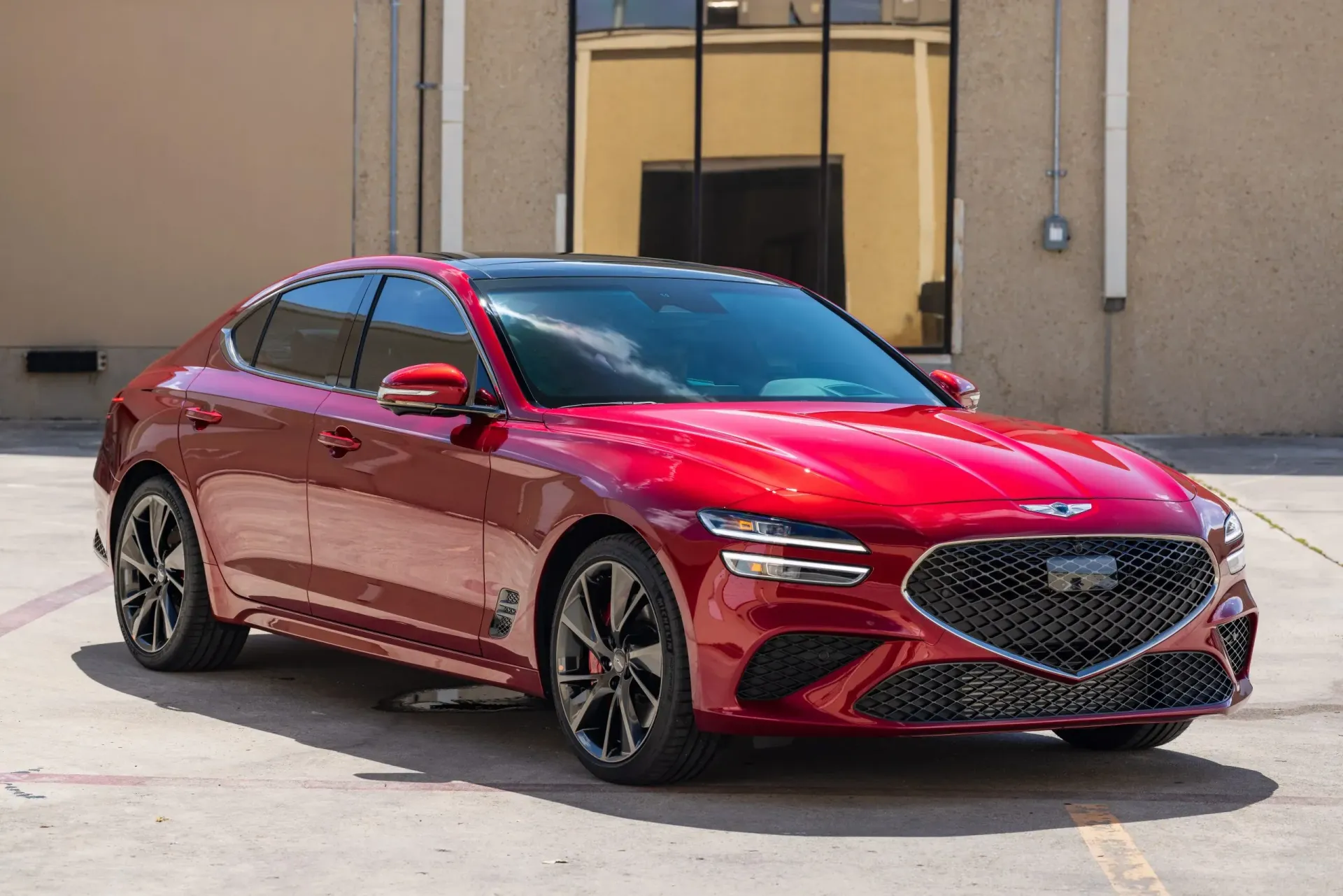 Red Genesis G70 sedan parked in front of a building.