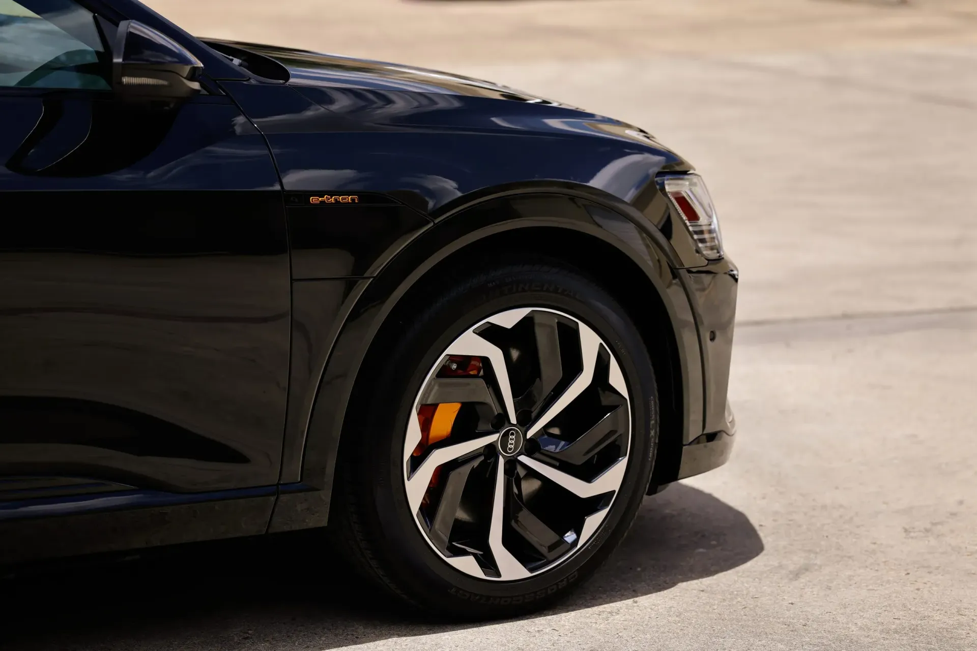 Black SUV, close-up of the front wheel with a distinctive black and white rim design and orange brake caliper.