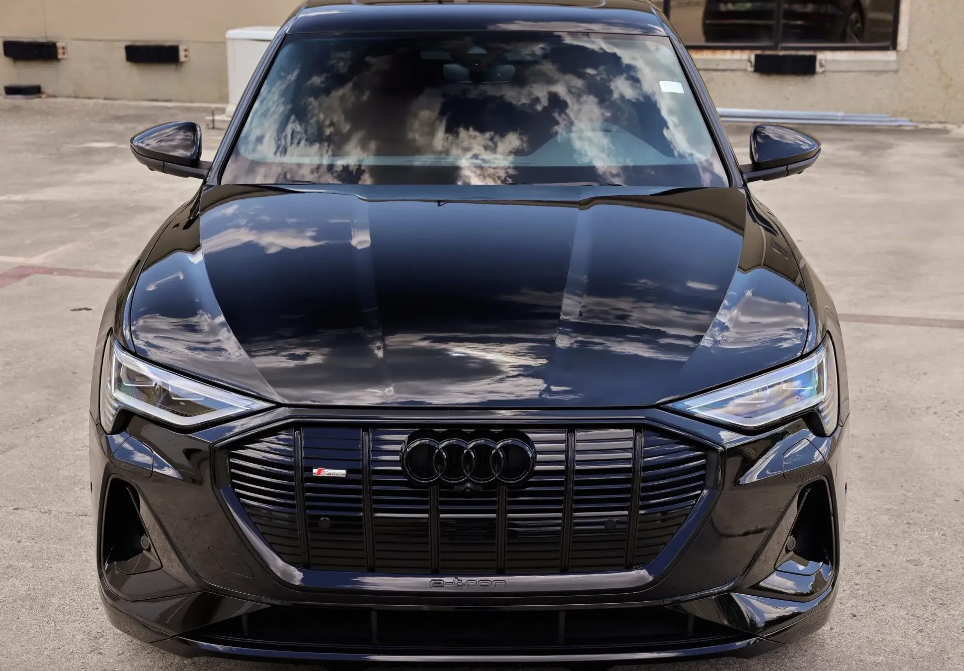 Black Audi e-tron SUV with glossy hood, black grille, and visible cloud reflections.