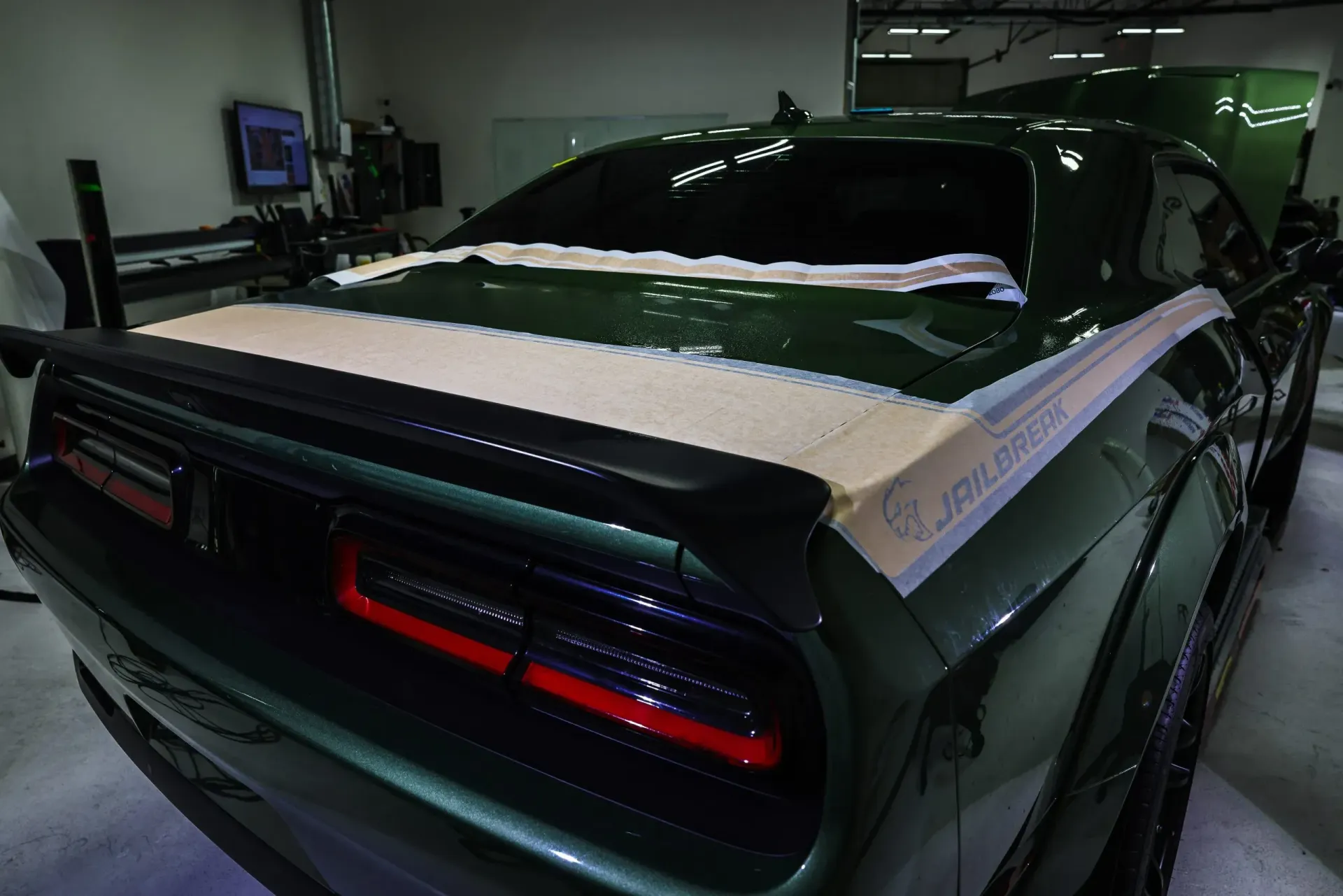Dark green Dodge Challenger with white stripes being worked on in a shop.