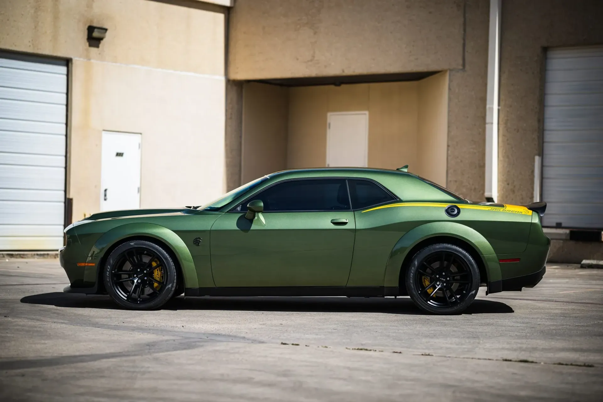 Green Dodge Challenger sports car parked near a building.