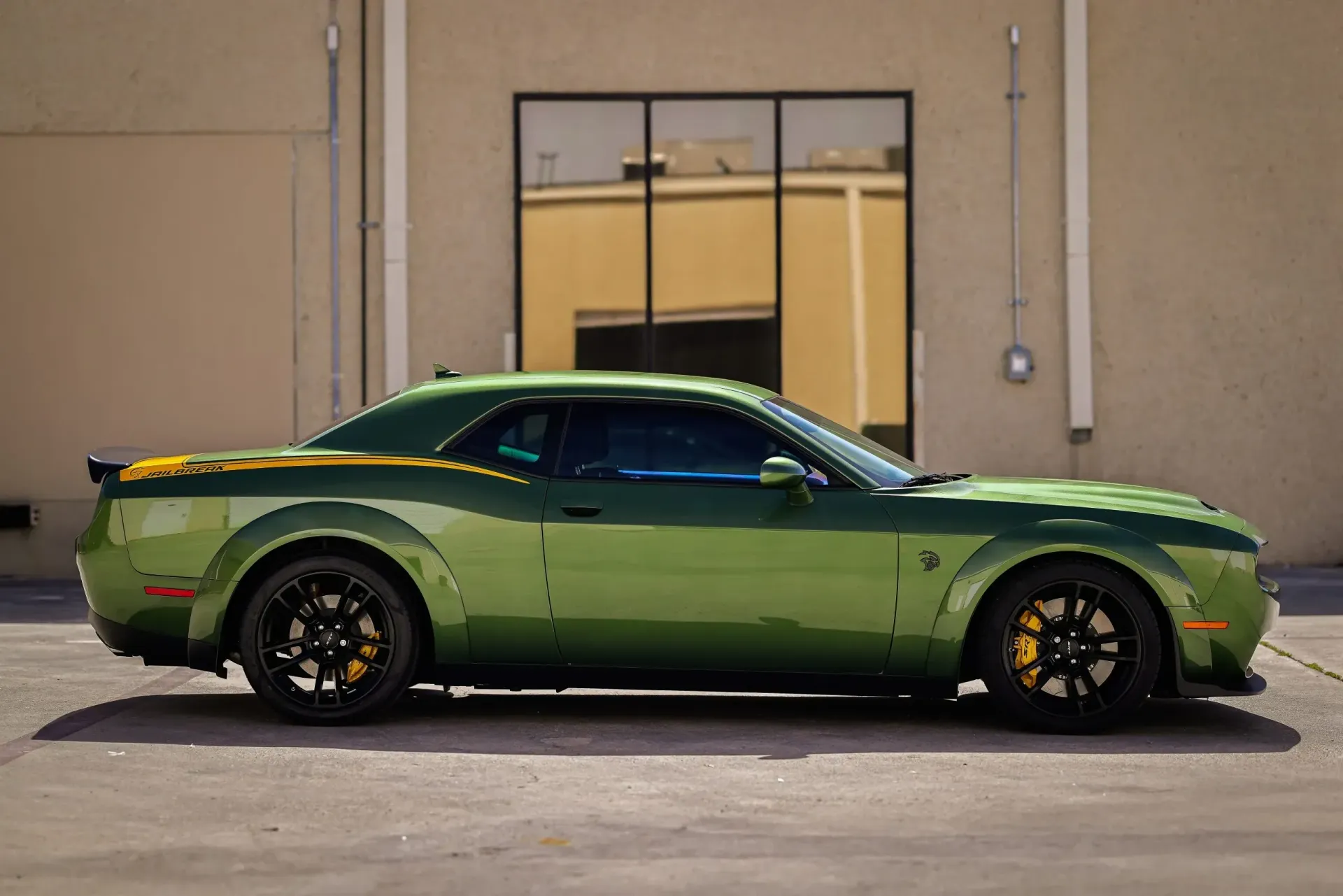 Green Dodge Challenger parked outside a building with black wheels and yellow brake calipers.