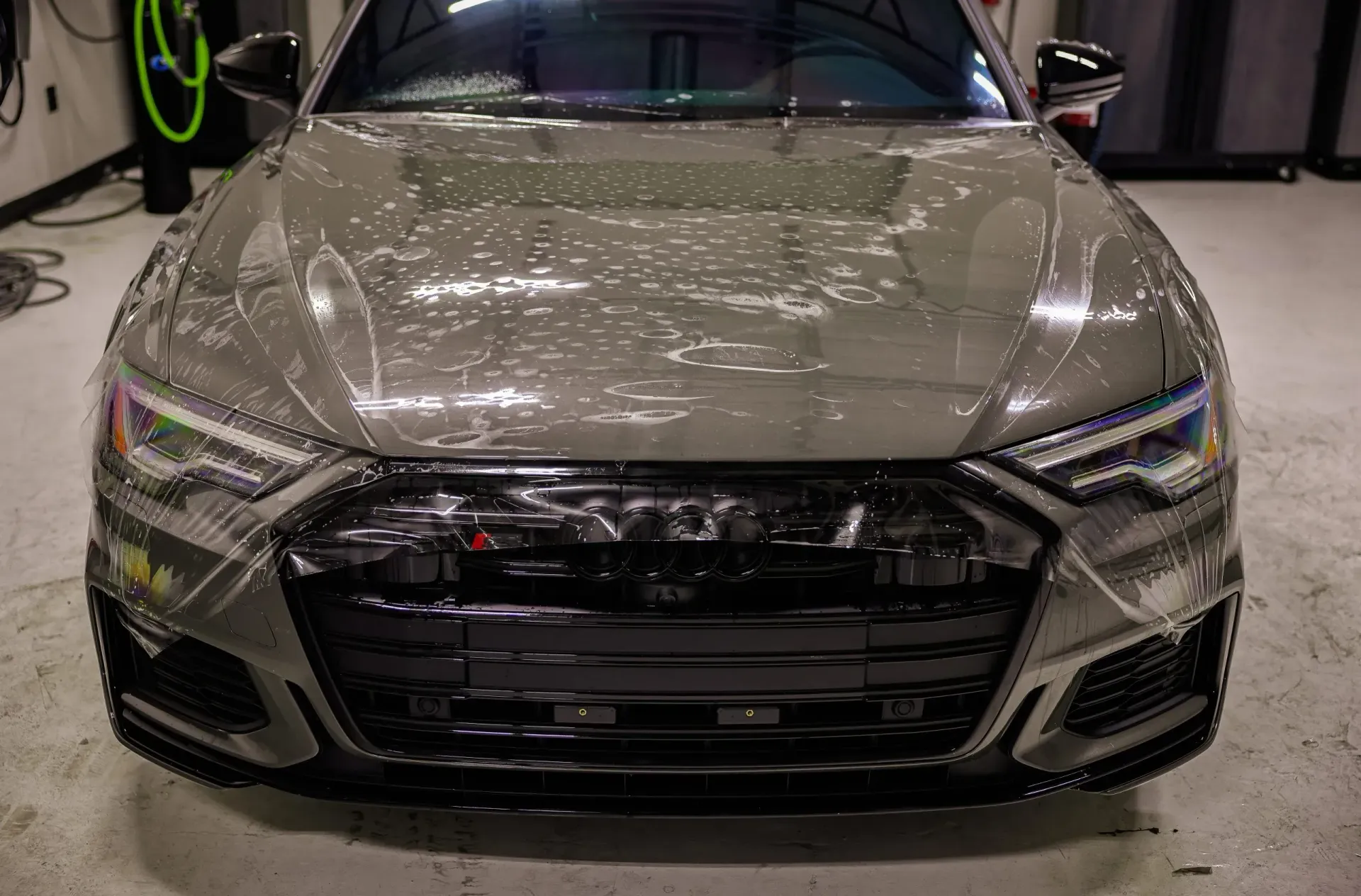Gray Audi sedan, front view, covered in water or foam, in a garage setting.